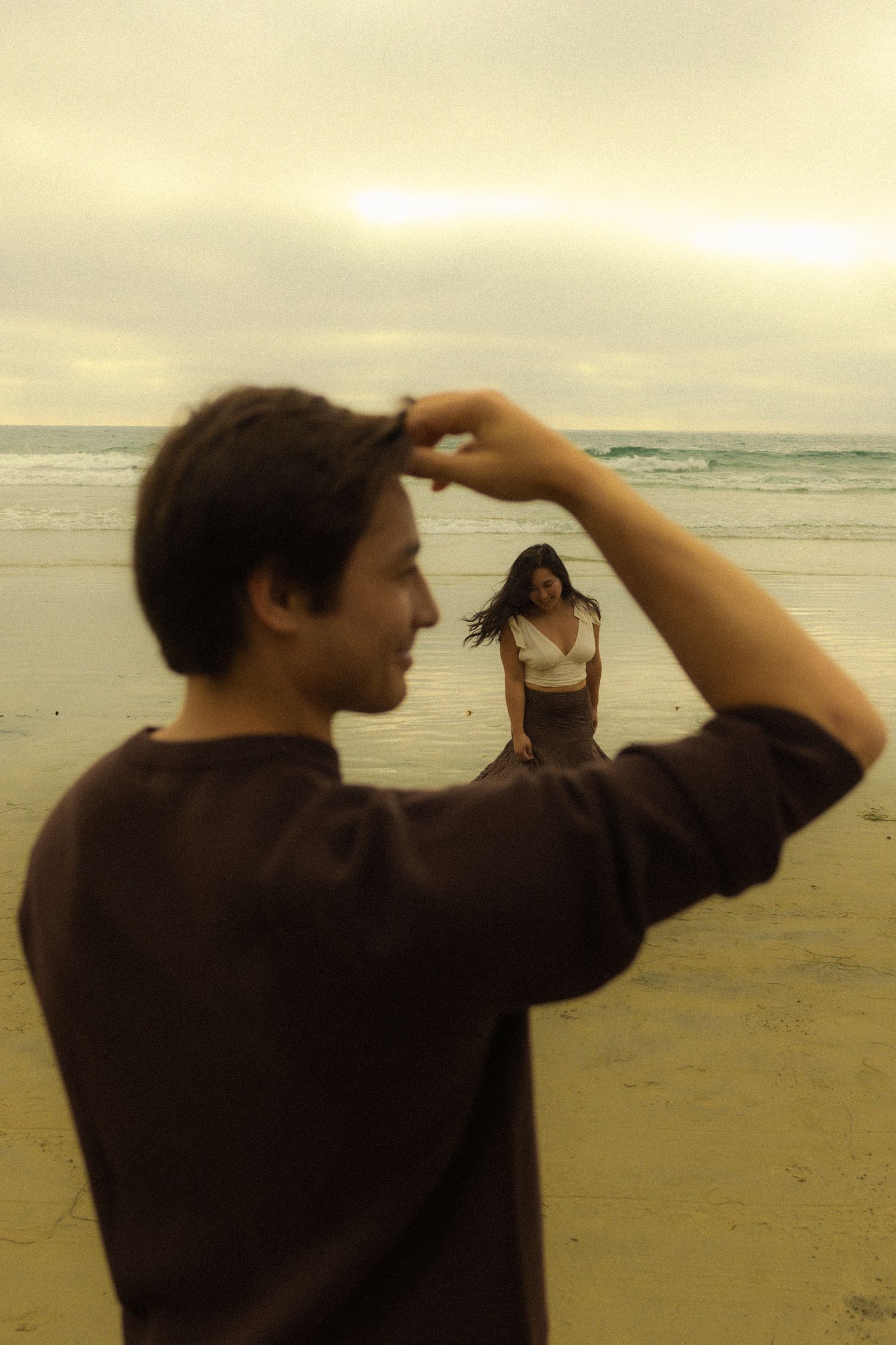 A person in dark clothing stands on a beach at sunset looking out towards the ocean horizon.