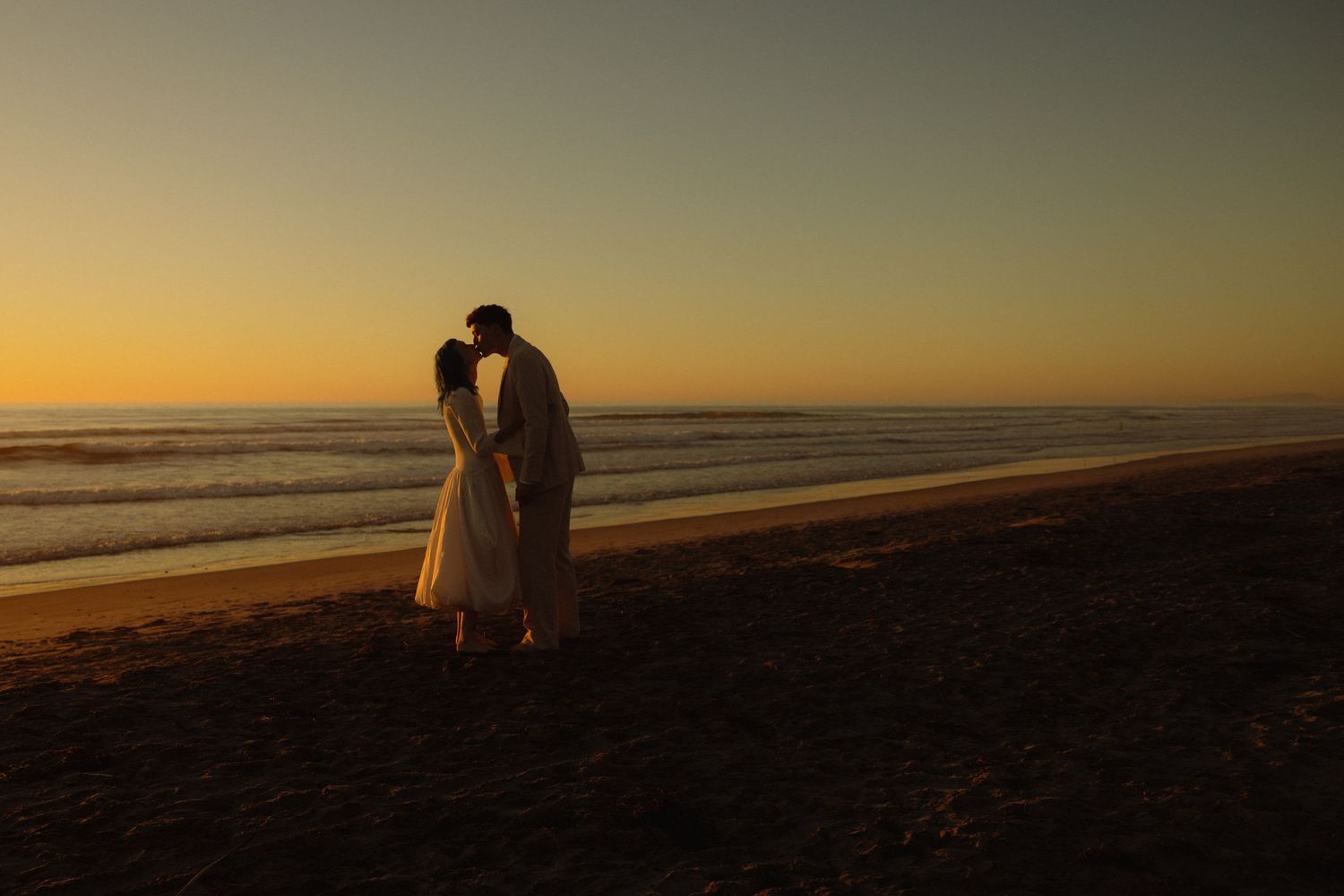 A silhouetted couple embraces on a beach at sunset with golden light reflecting off the ocean waves.