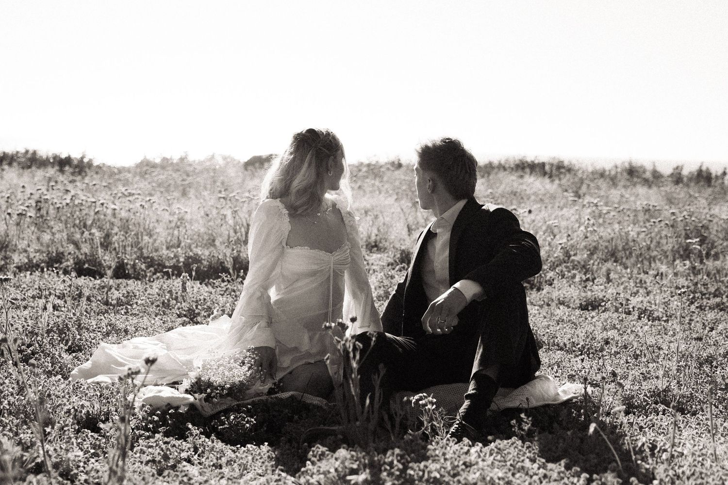 Black and white photo series showing a couple sitting together in a grassy meadow.