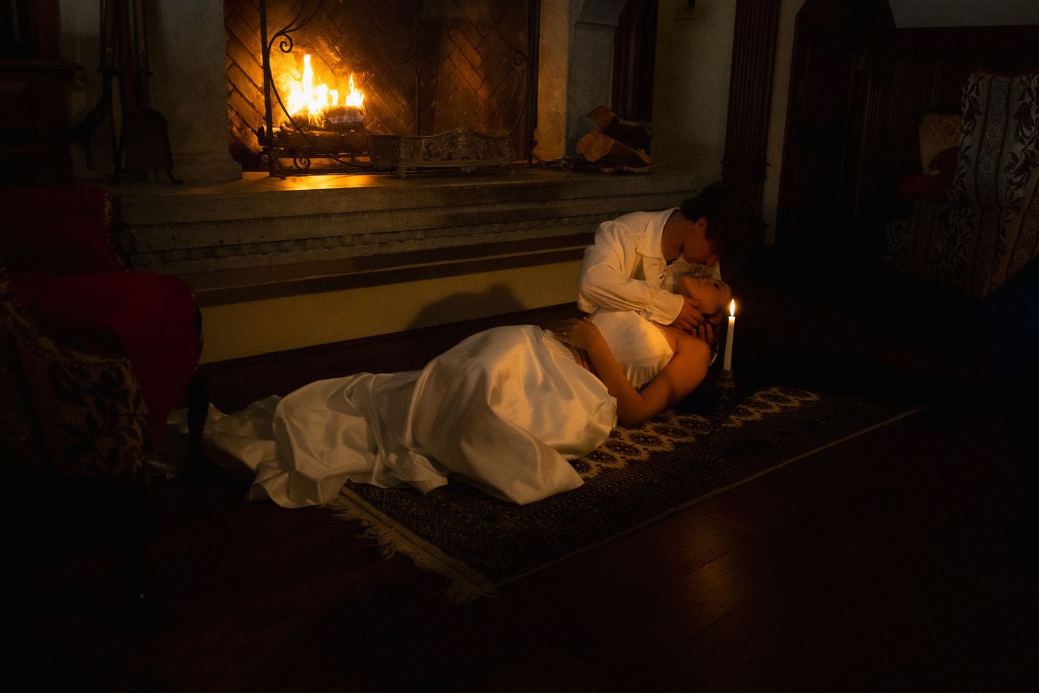 A romantic scene by firelight with a white-dressed figure reclining near a burning hearth.