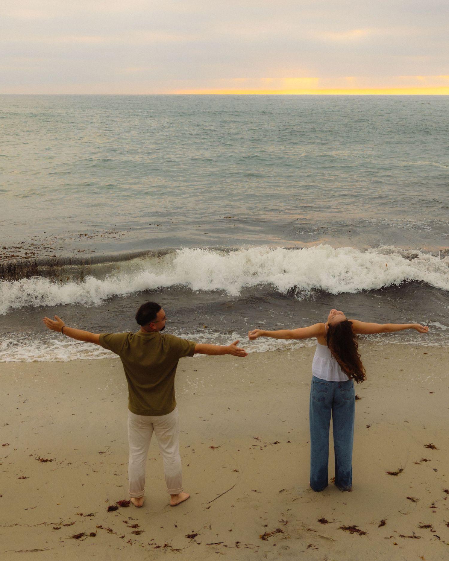 People standing with outstretched arms on a beach at sunset, creating a panoramic sequence of silhouettes against the ocean.