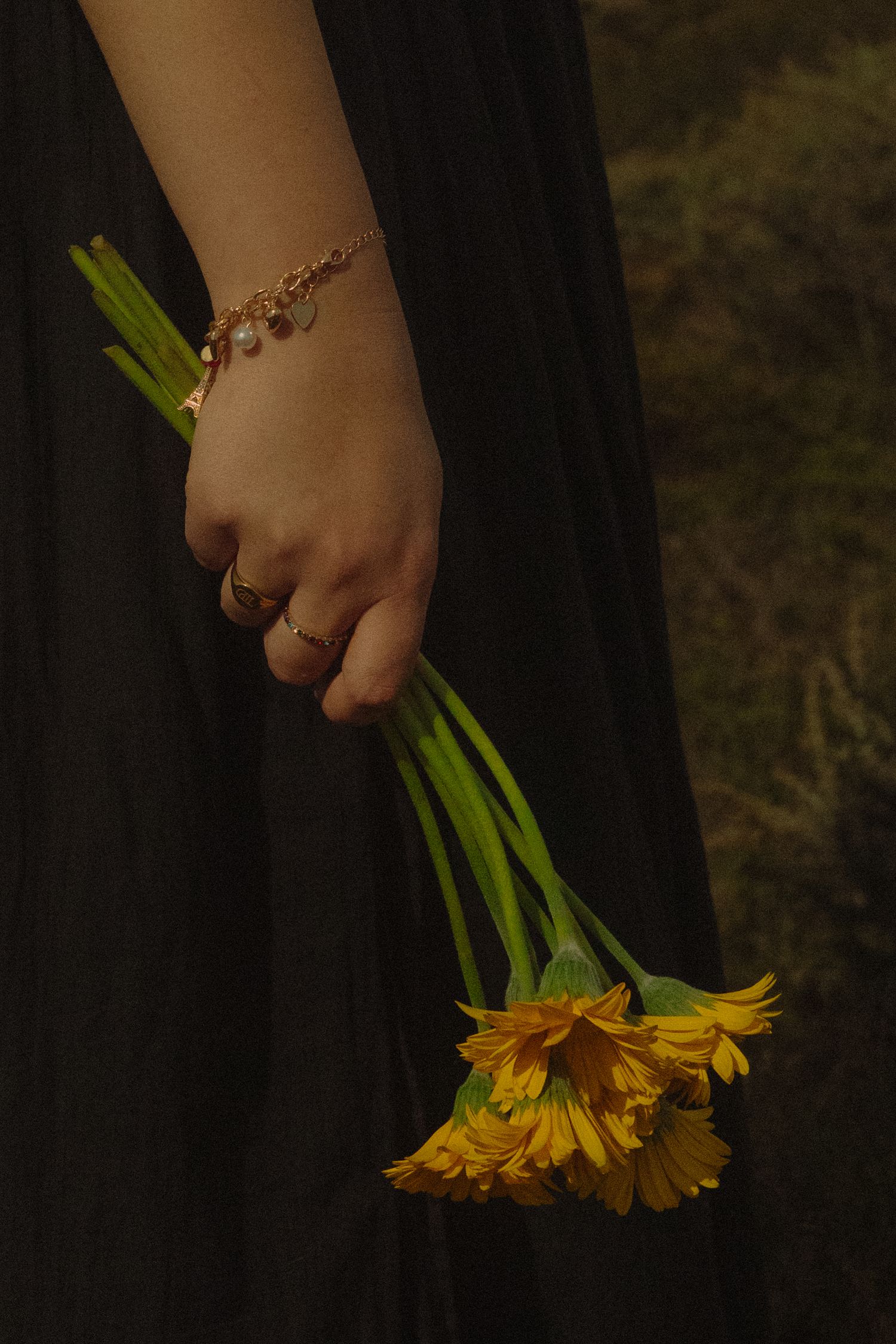A hand wearing a bracelet holds yellow daisies against a black dress background.