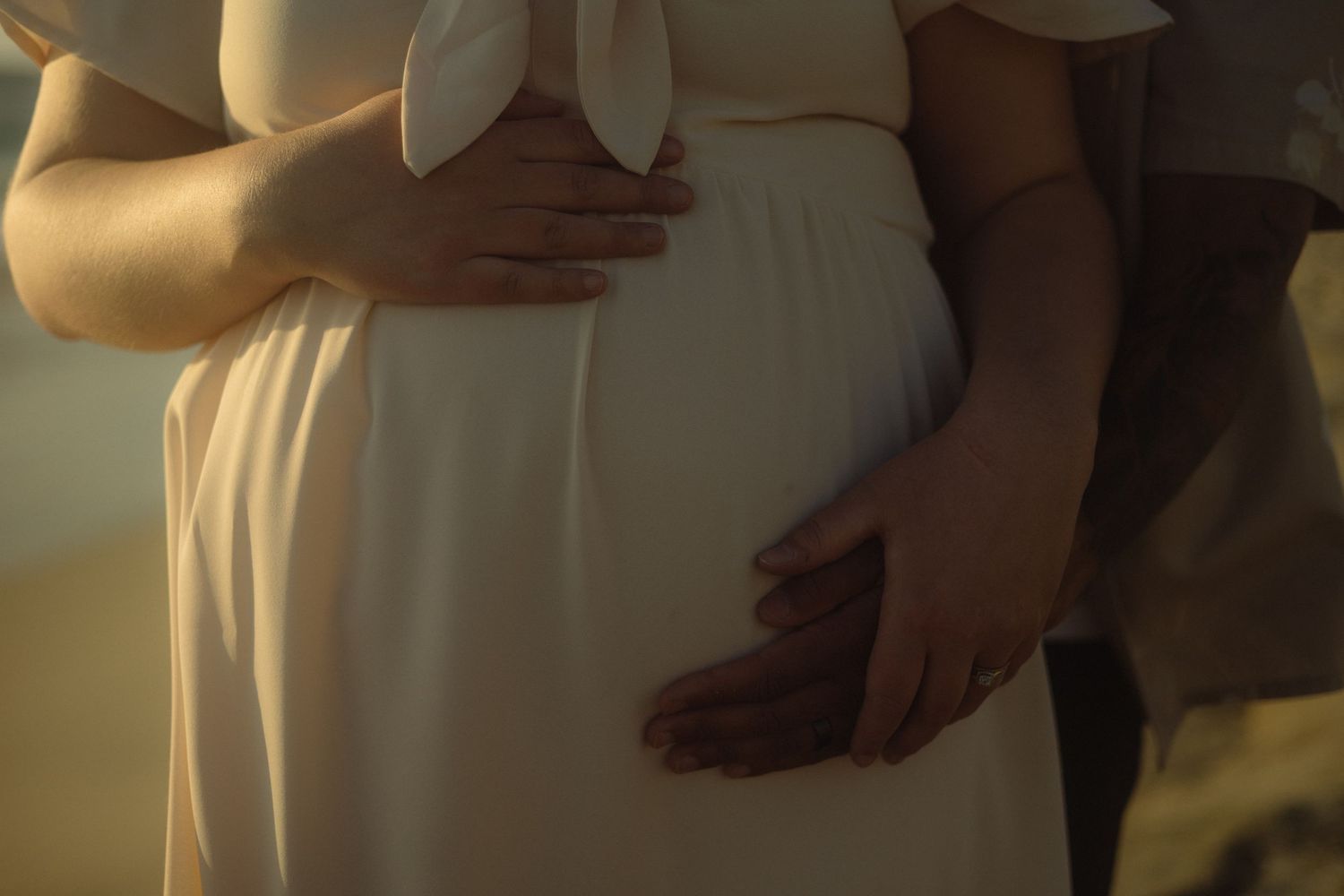 Close-up view of hands resting against a flowing white dress in warm, golden lighting.