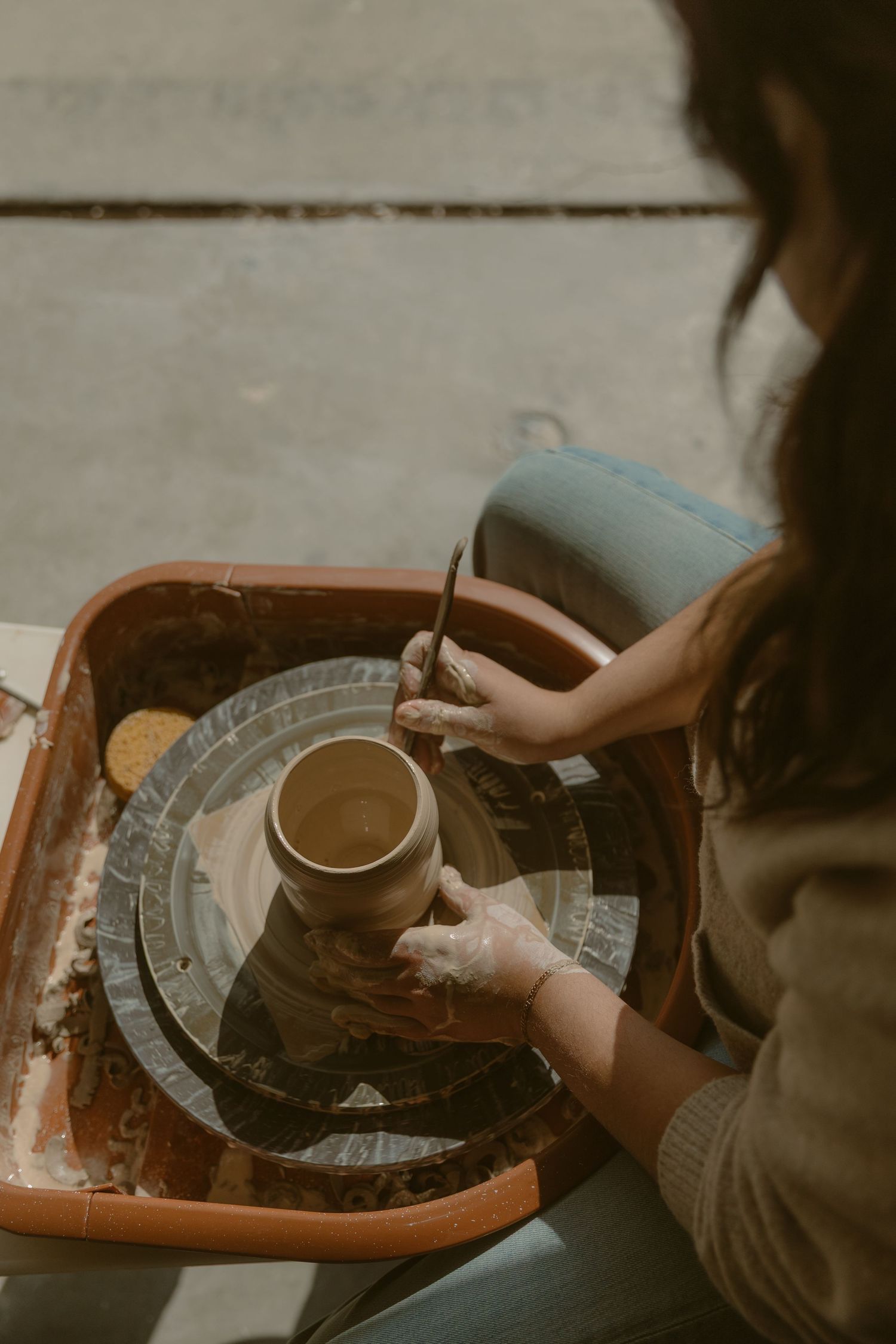 Hands working clay on a pottery wheel with a rustic brown glaze.