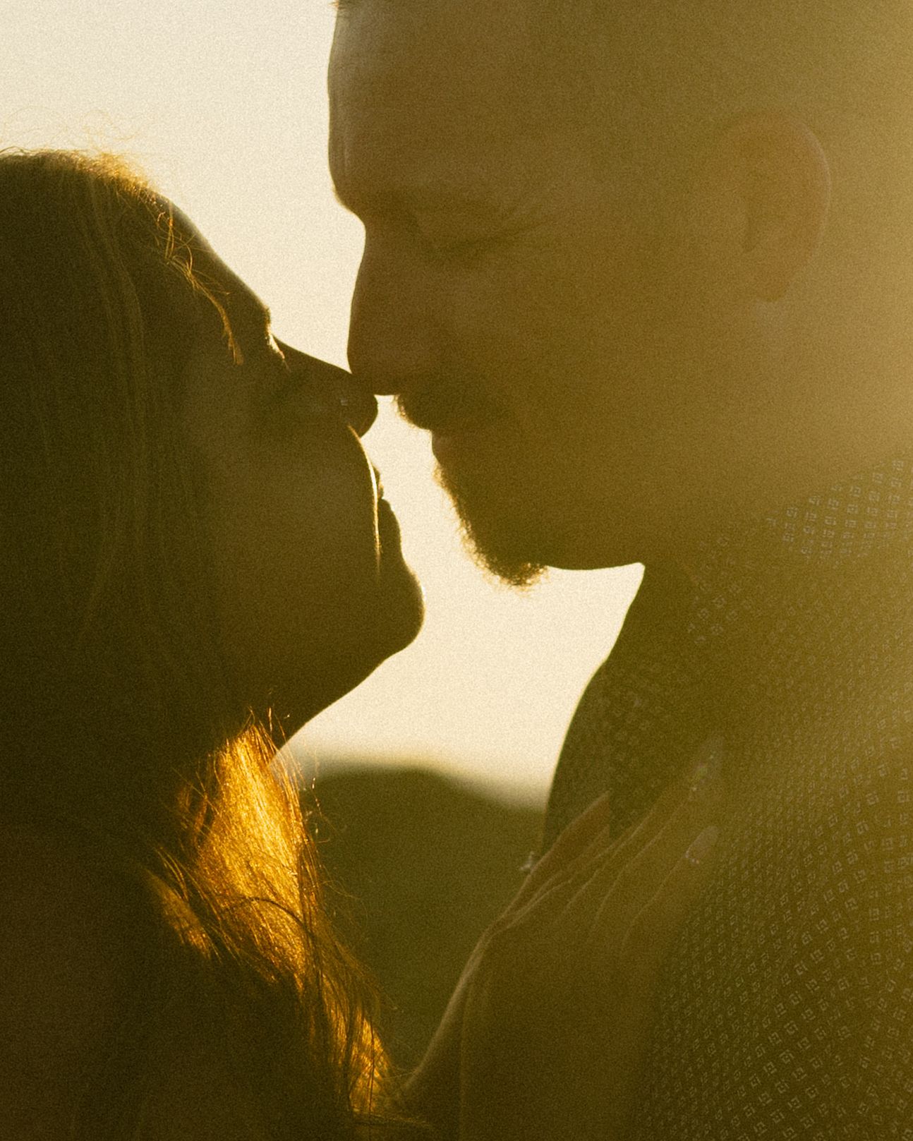 A silhouetted couple in a romantic pose at sunset with golden light illuminating their profiles.