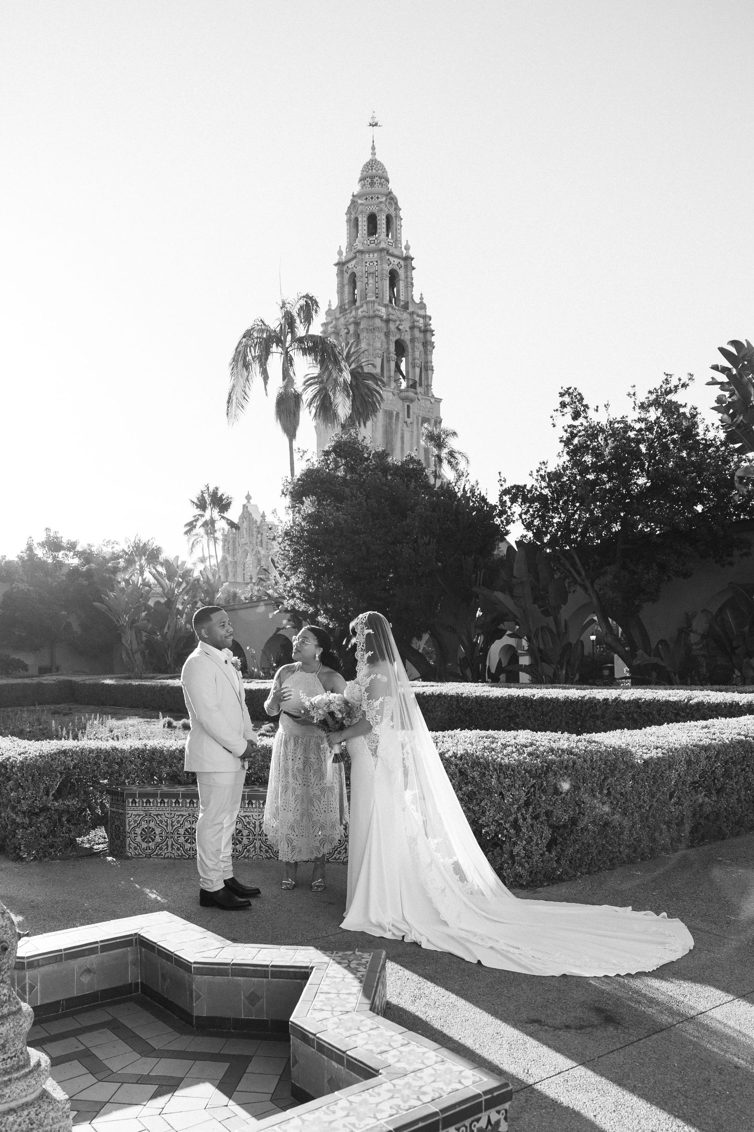 Black and white wedding ceremony photo at Balboa Park San Diego with bride groom and officiant by ornate fountain tower backdrop.