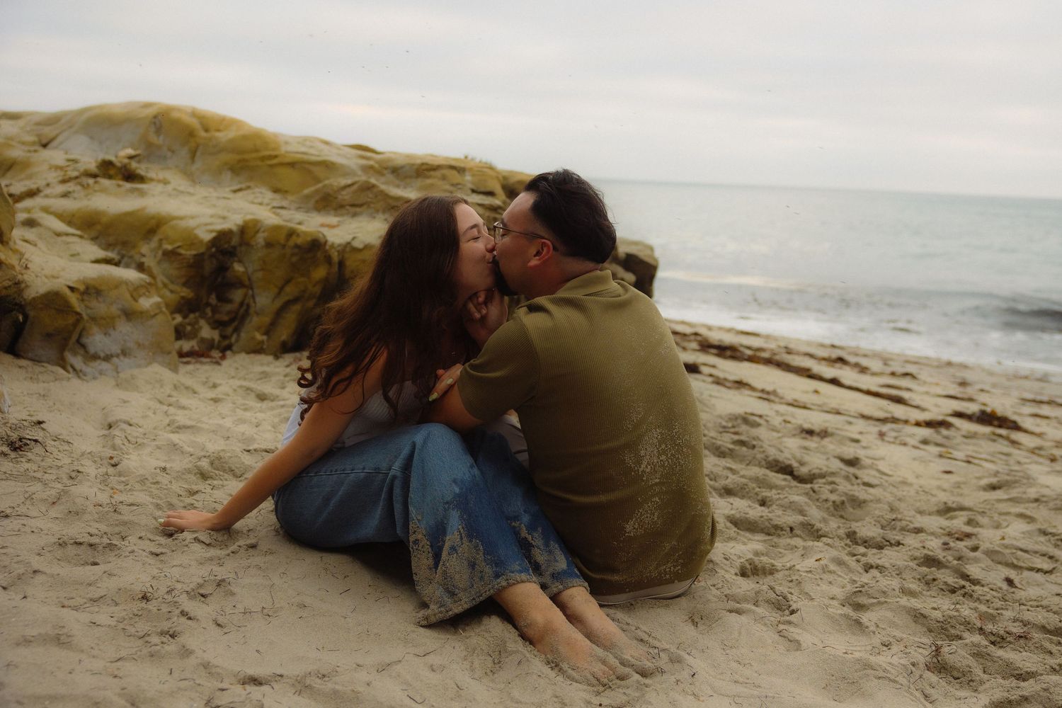A couple shares a tender moment together on a sandy beach during sunset.