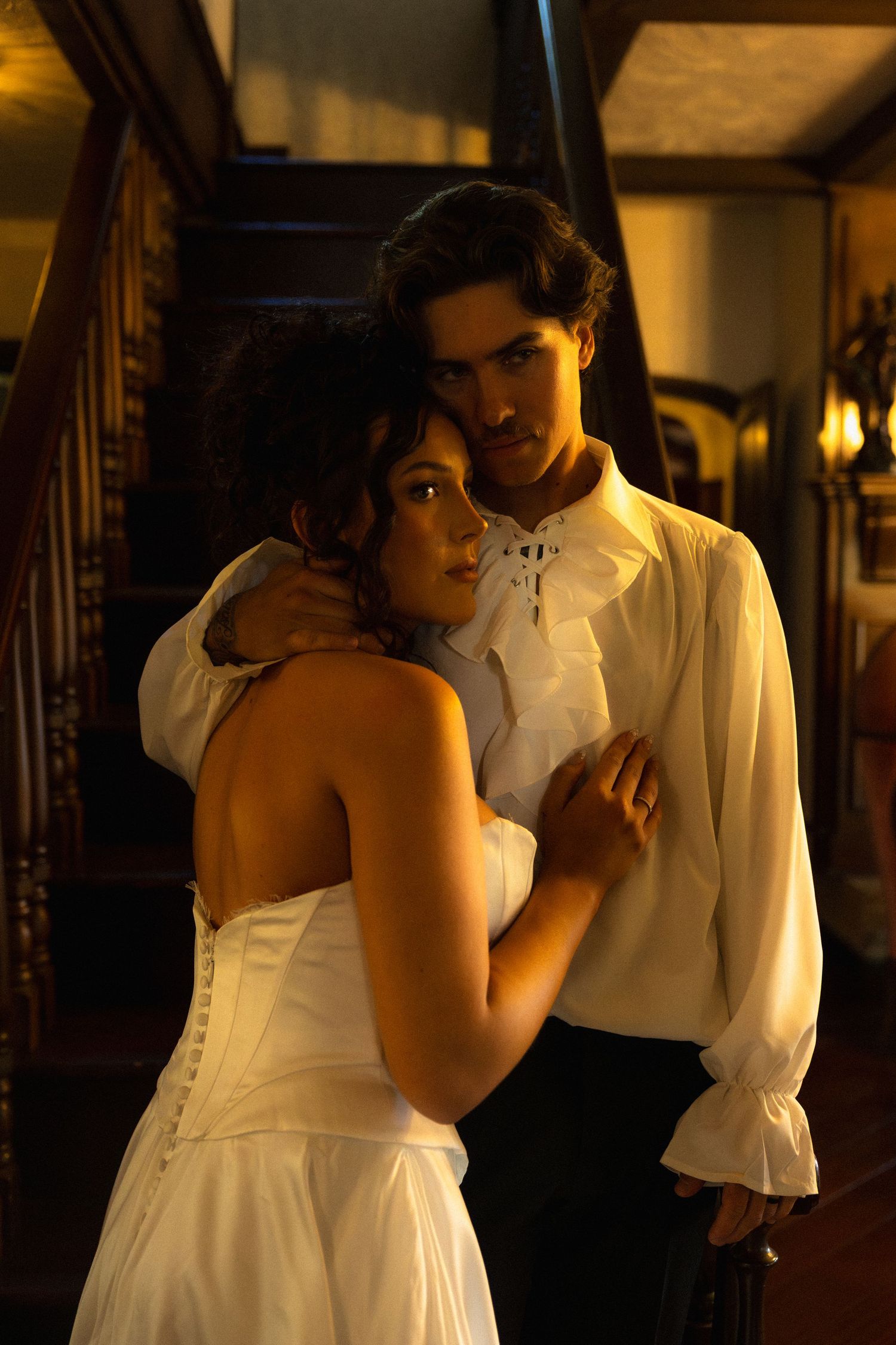 Intimate scene captured in warm candlelight with figures in white formal attire.