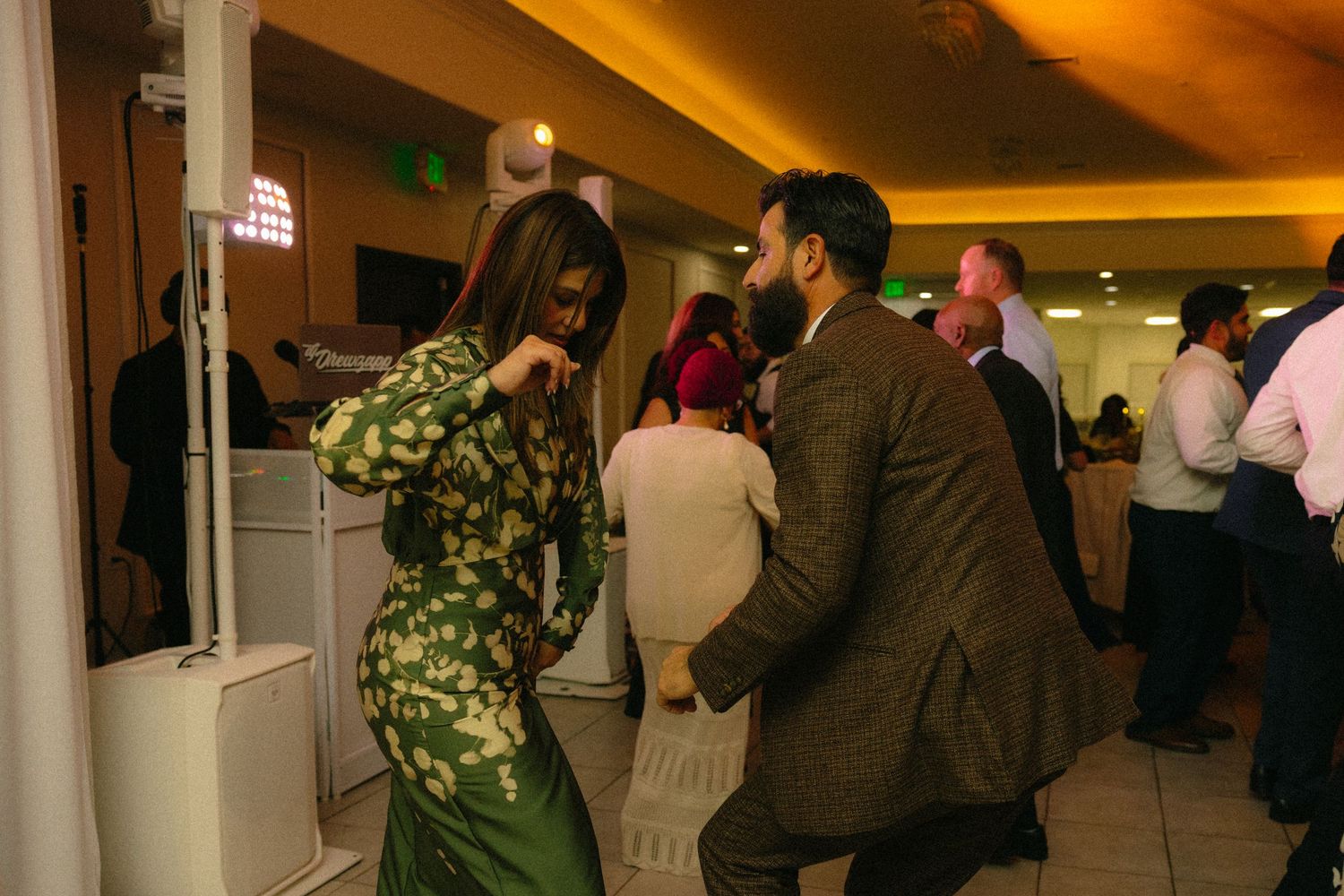 Guests enjoying a festive celebration in an amber-lit banquet hall with decorative columns.