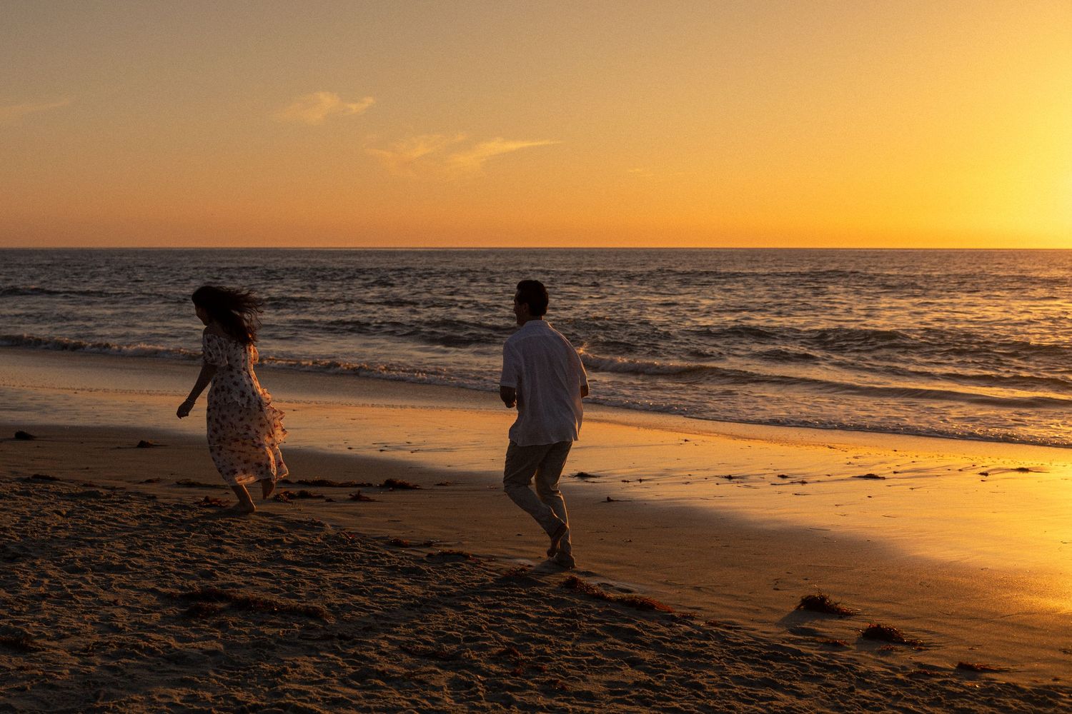 Silhouettes of beachgoers walking along the shoreline during a vibrant orange sunset over the ocean.