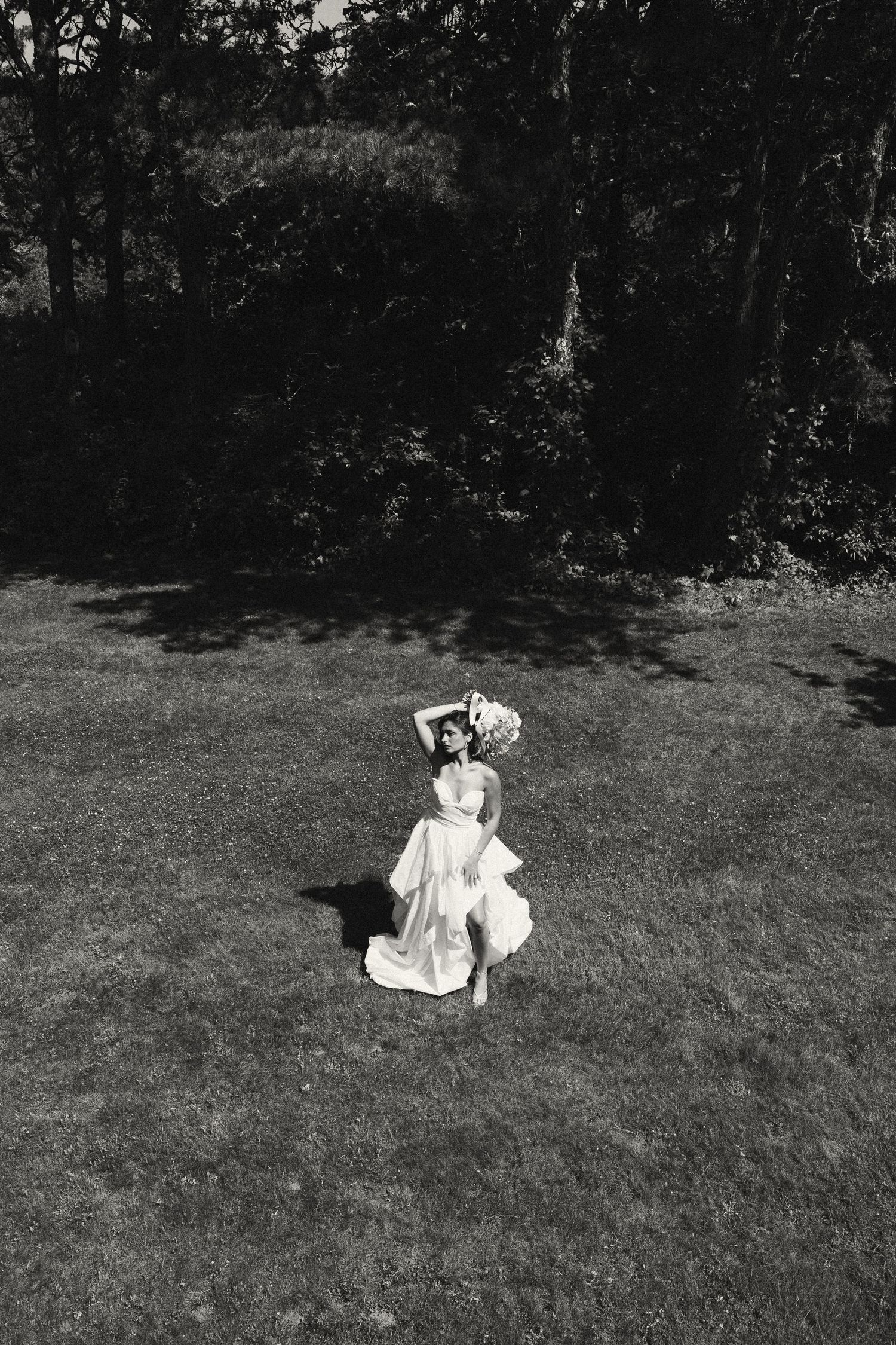 Black and white photo of a bride in a flowing white gown running across a sunlit lawn with trees in the background.