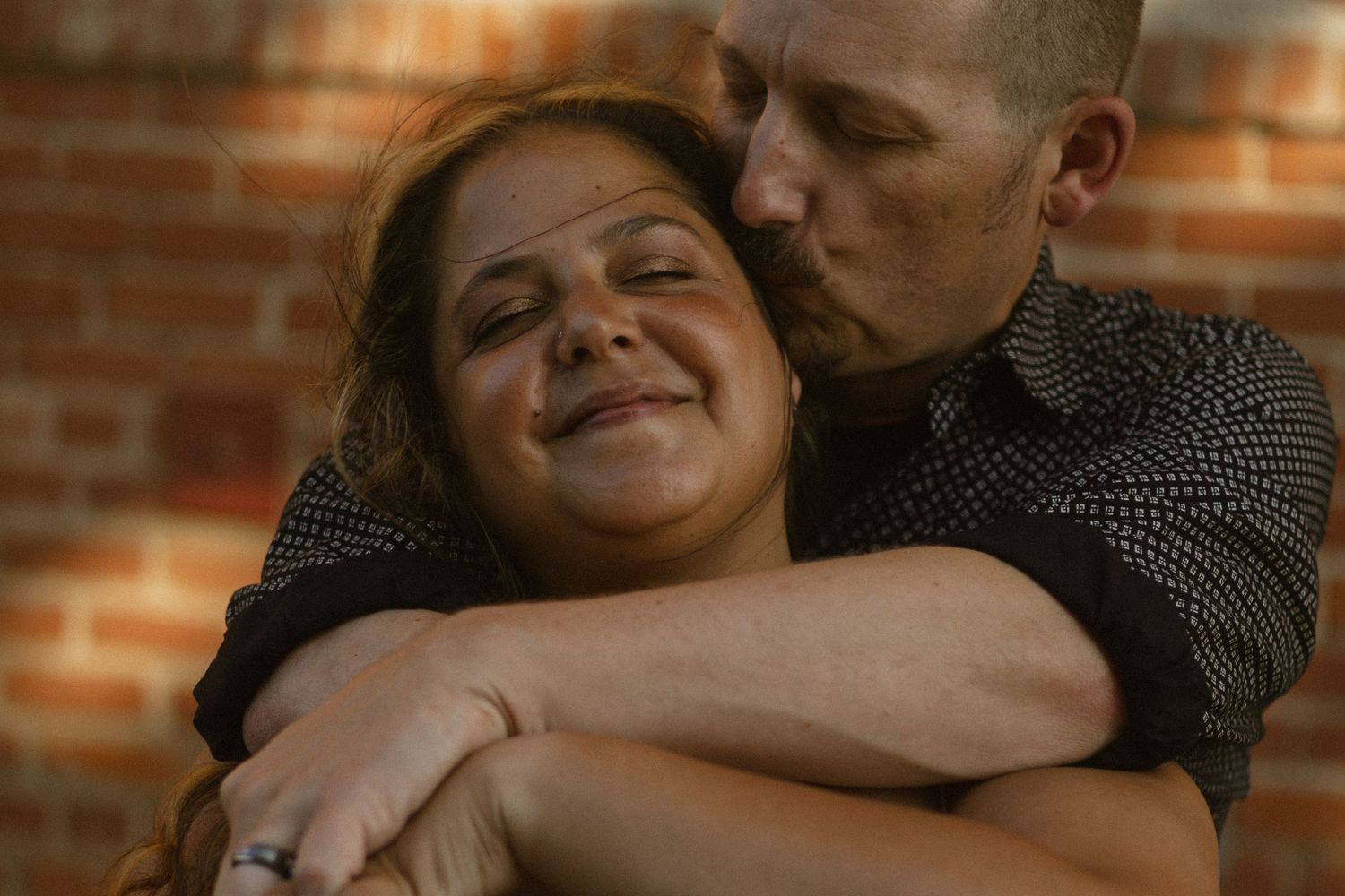 A happy couple shares an intimate moment together against a rustic brick wall background.