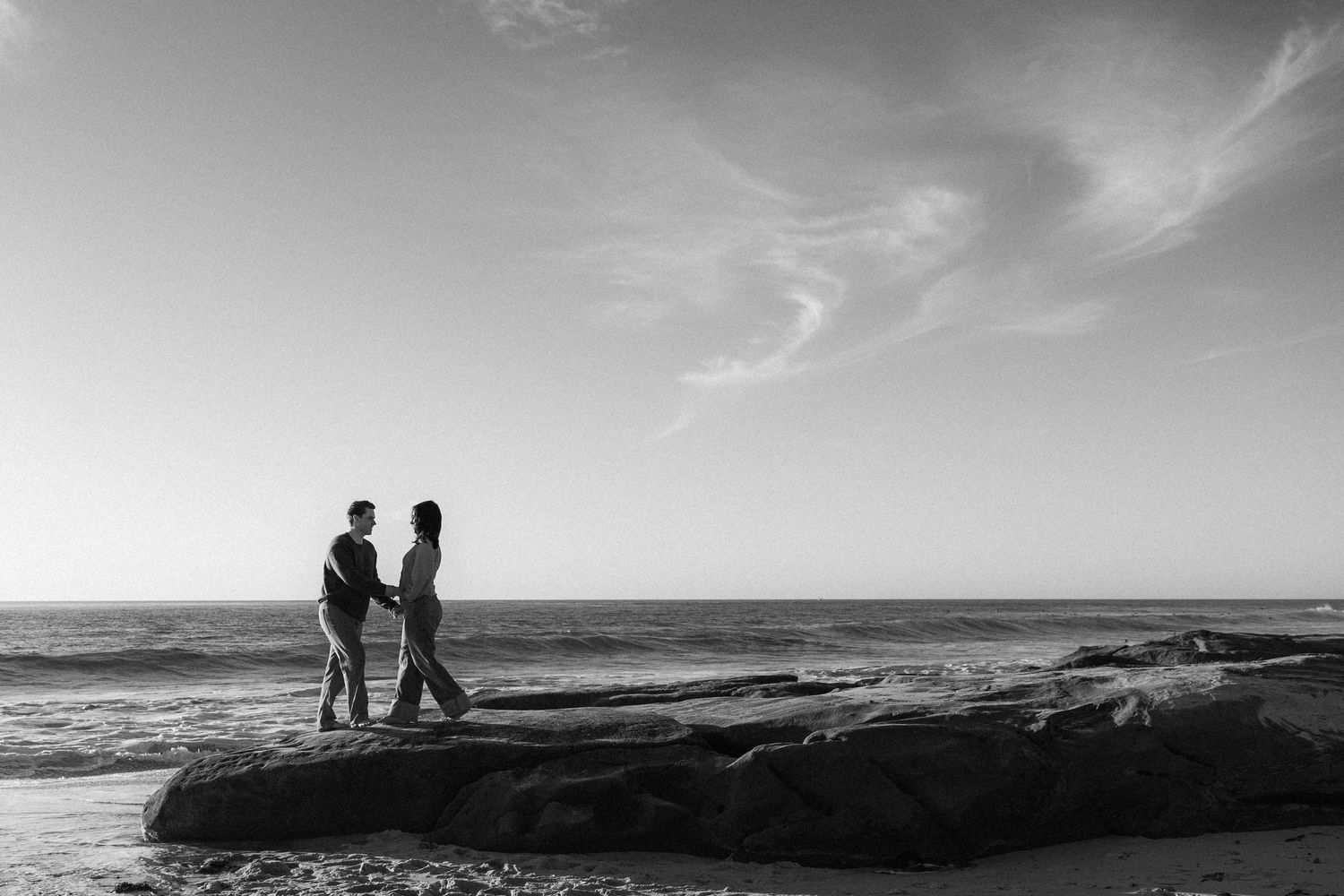 A black and white panoramic series of beach landscapes showing silhouetted figures against dramatic cloudy skies.