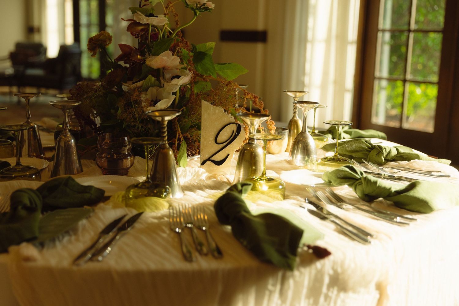 Sunlight streams through windows onto a dining table set with elegant white dishes and floral arrangements.