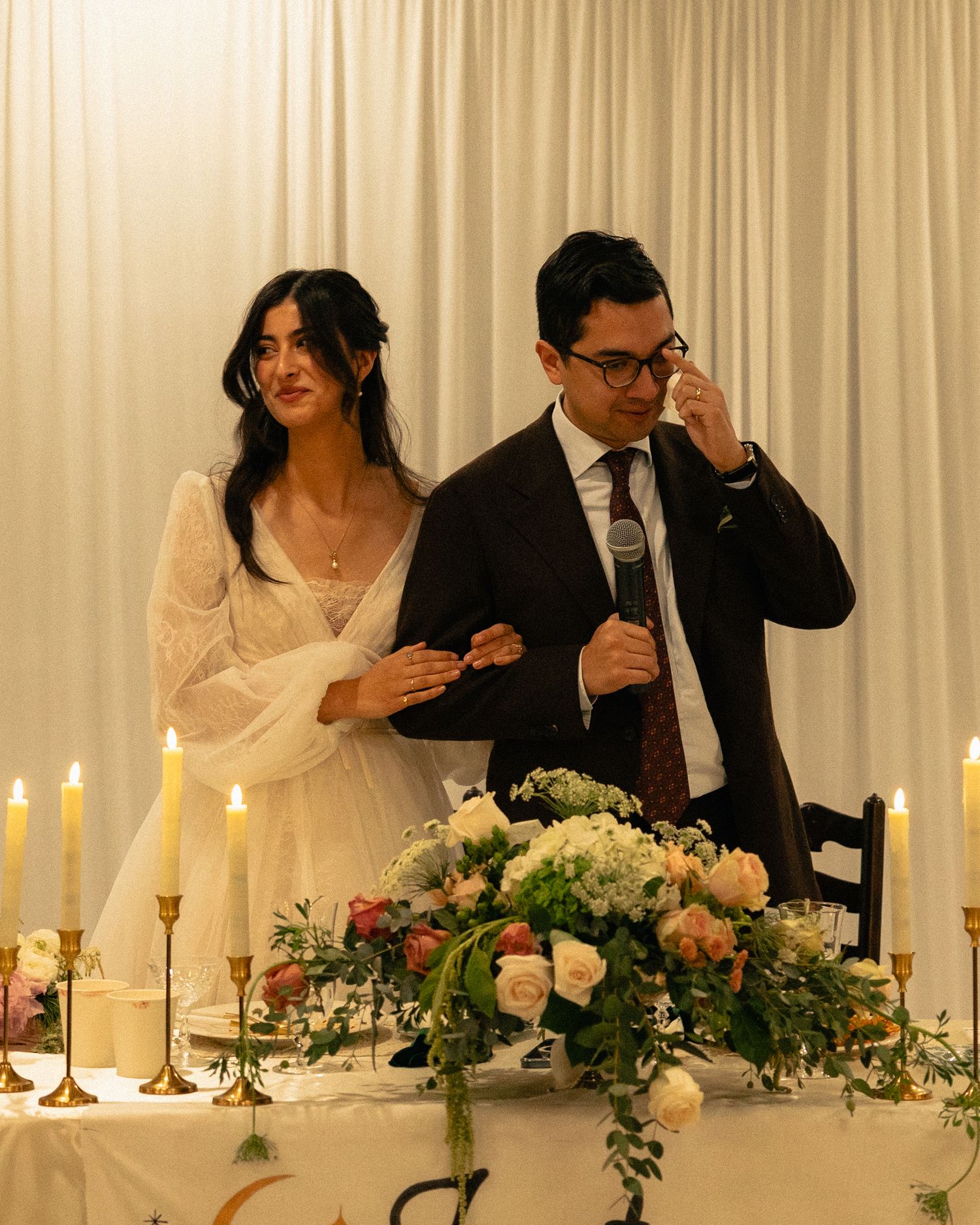 Elegant wedding reception table decorated with white candles and floral arrangements against a light backdrop.