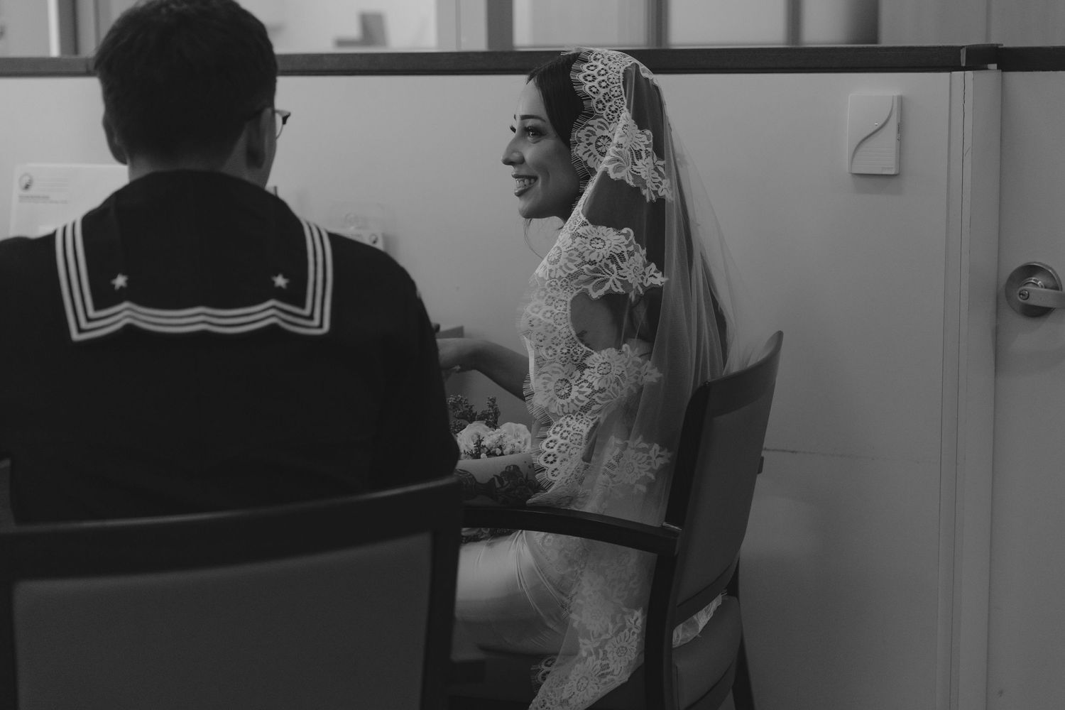 Black and white photo showing a sailor and bride sitting indoors at a table during what appears to be a wedding event.