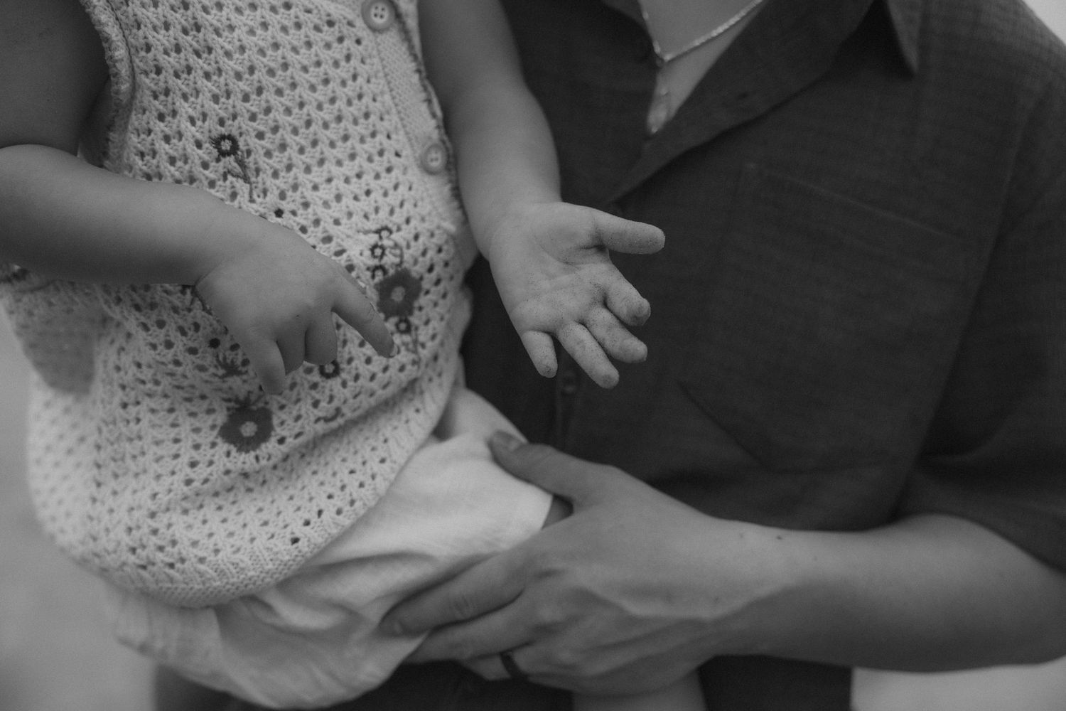 A baby's hand reaches out to grasp an adult's finger in a tender black and white photograph.