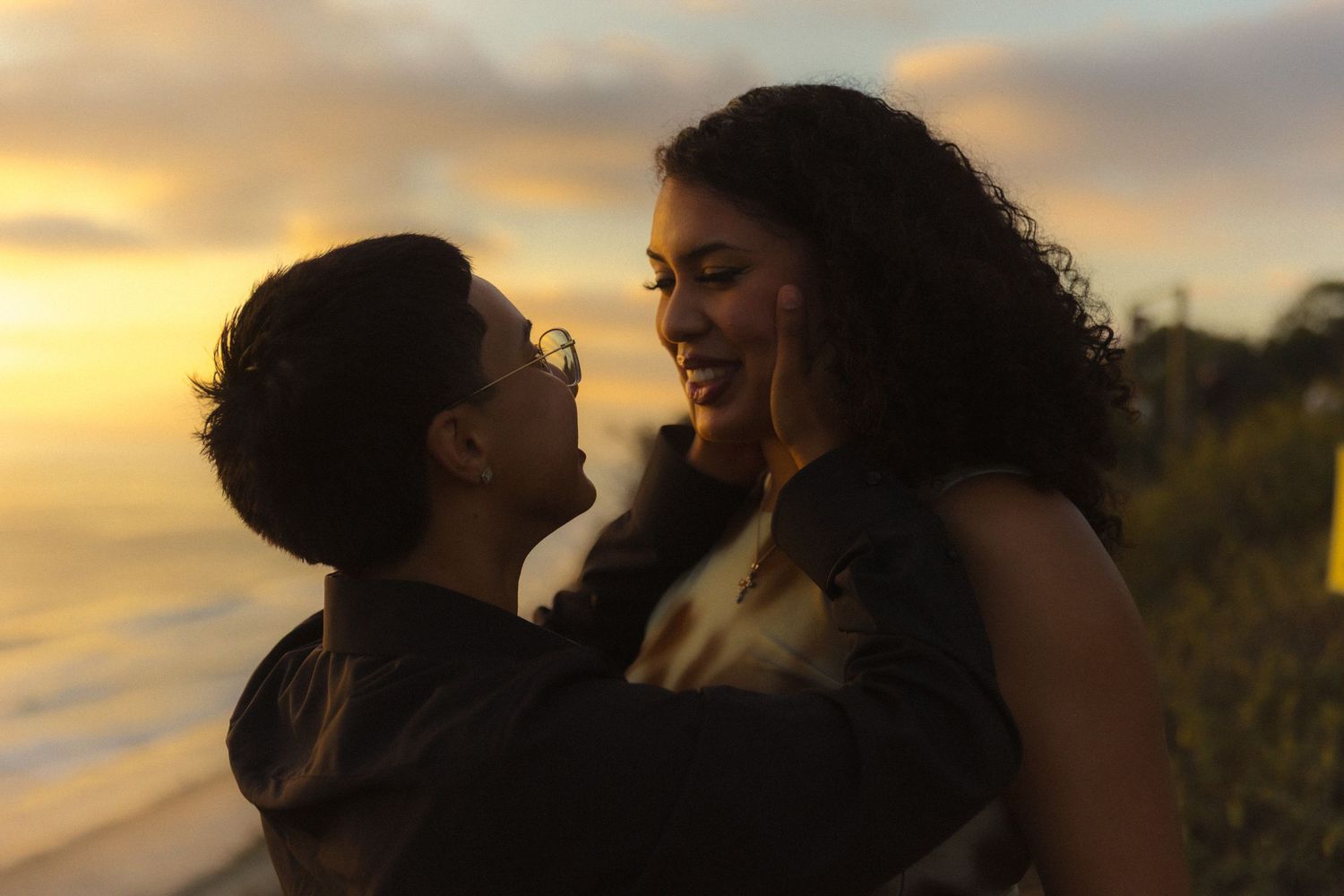 A couple shares a romantic moment against a golden sunset sky on a coastal overlook.