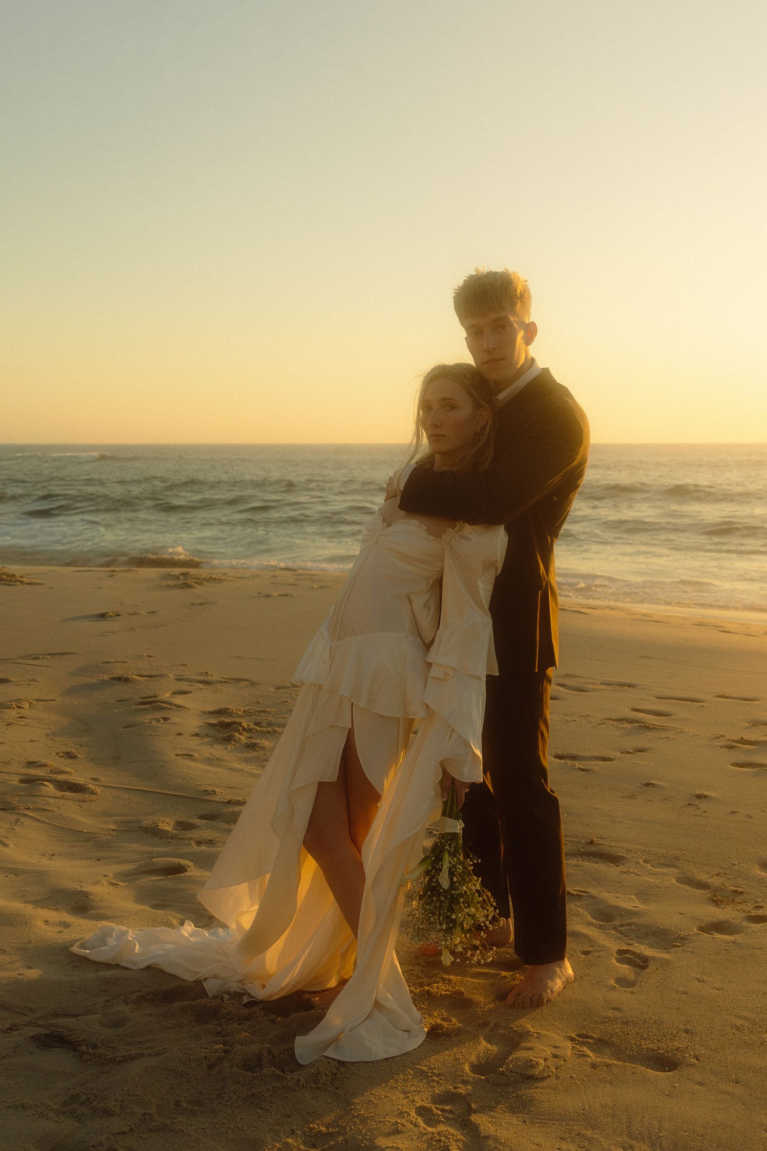 A couple embraces on a sandy beach at sunset creating a romantic silhouette against the golden sky.