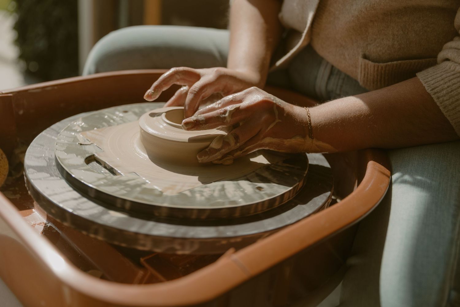 Close-up of hands shaping clay on a brown pottery wheel.