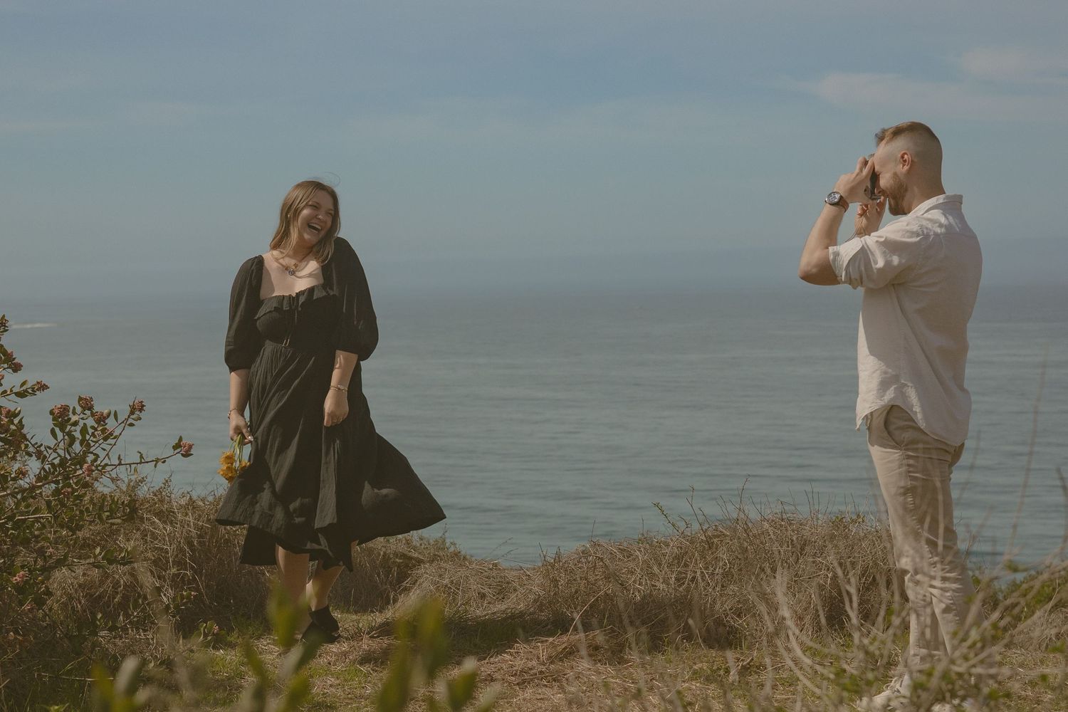Couple taking photos together on scenic coastal overlook.