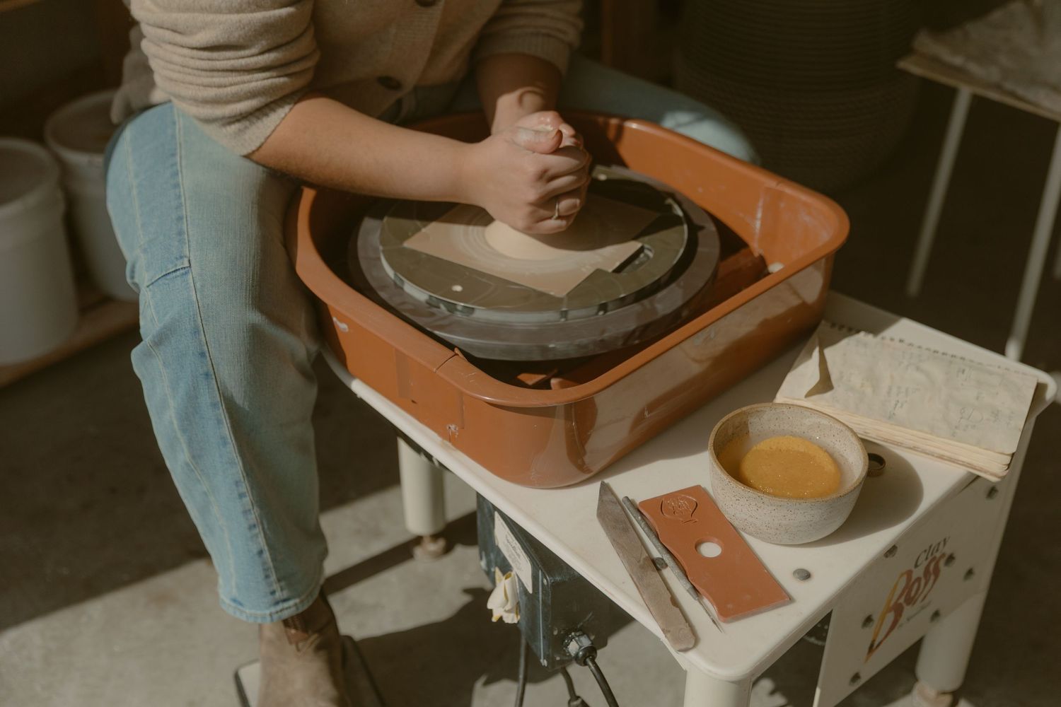 Potter working at wheel station with terracotta colored basin and white table for a ceramics branding session