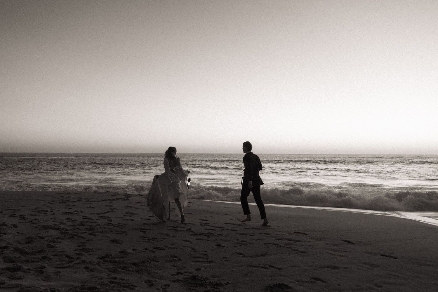 Person on horseback and runner on a misty beach at dusk in black and white.