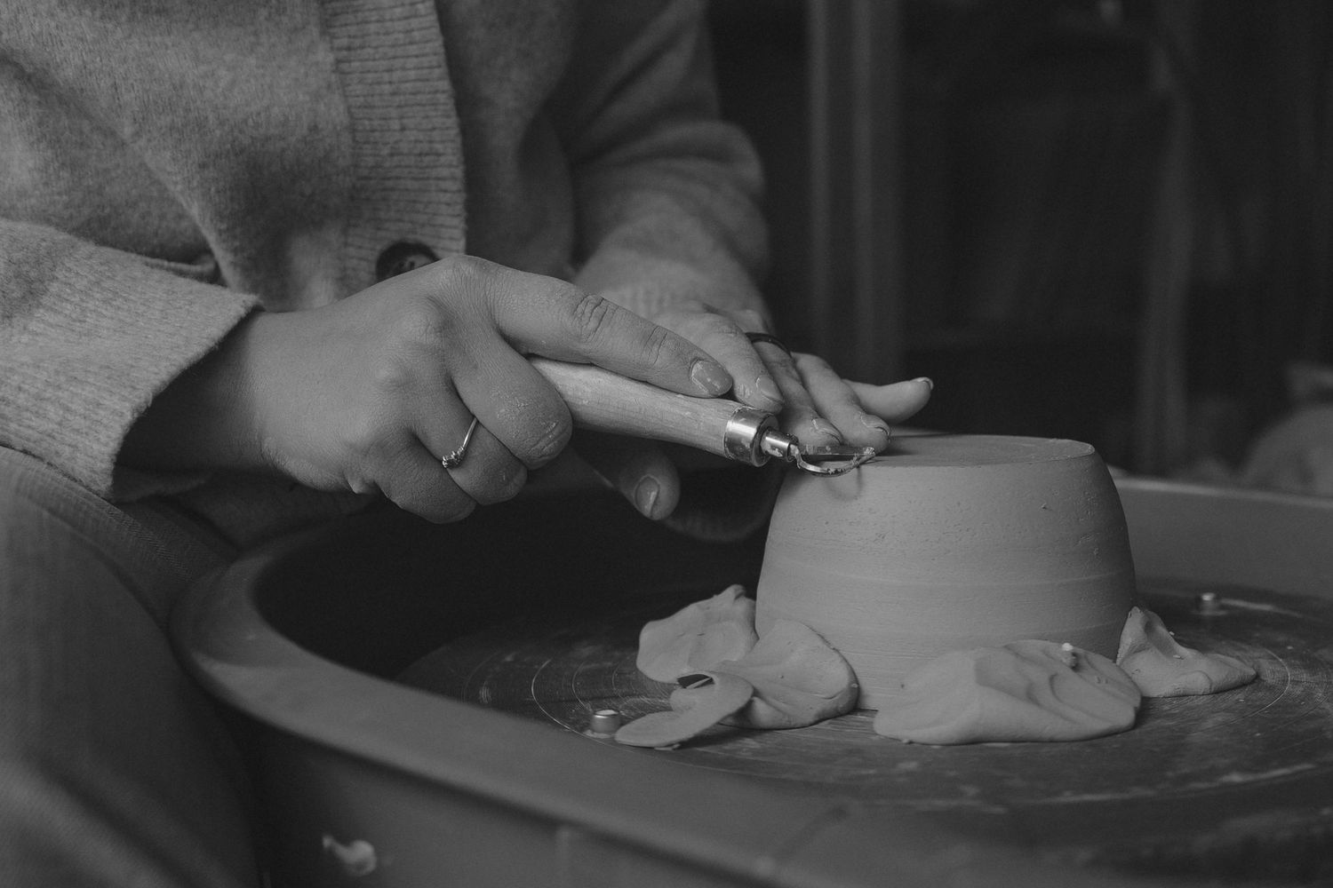 Hands working clay on a pottery wheel in black and white.
