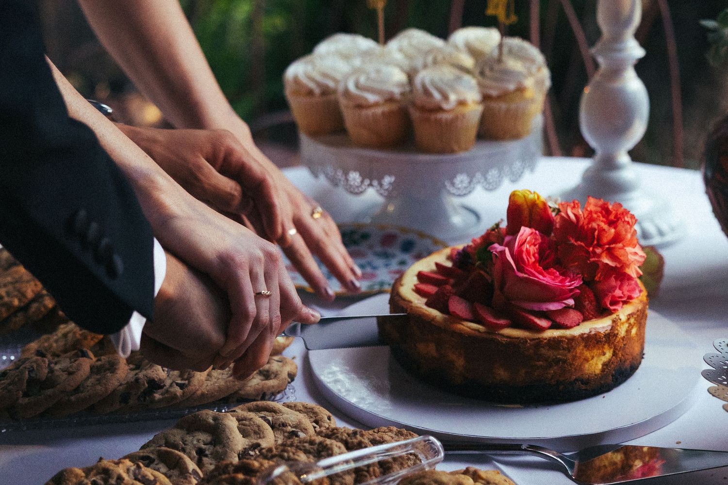 Assorted dessert table featuring a decorated cheesecake, cookies, and cupcakes being served at a celebration.