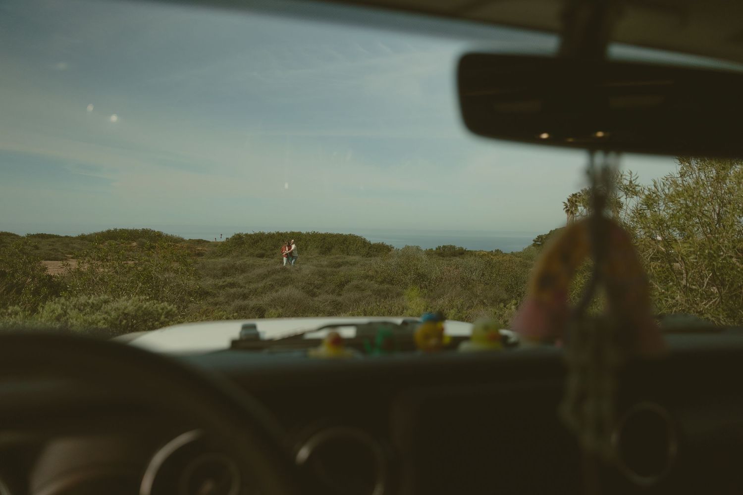A scenic coastal landscape view captured through a car windshield with dashboard visible.