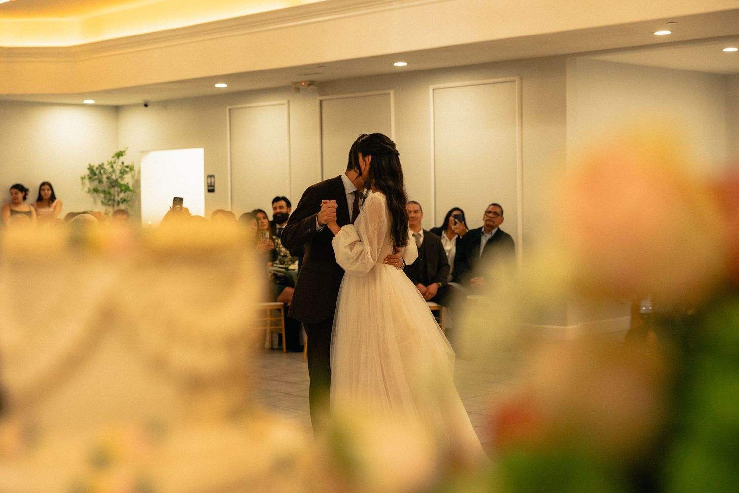 A wedding ceremony takes place in an elegant indoor venue with soft lighting and floral decorations.