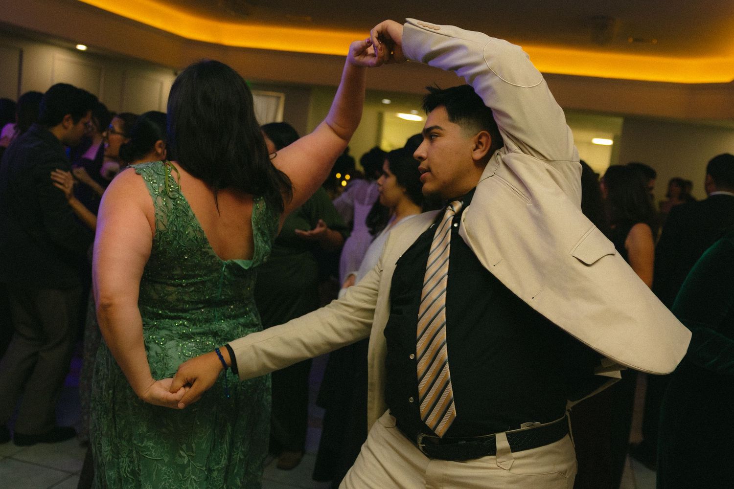 Crowd of partygoers dancing and mingling on a dance floor with yellow accent lighting above.