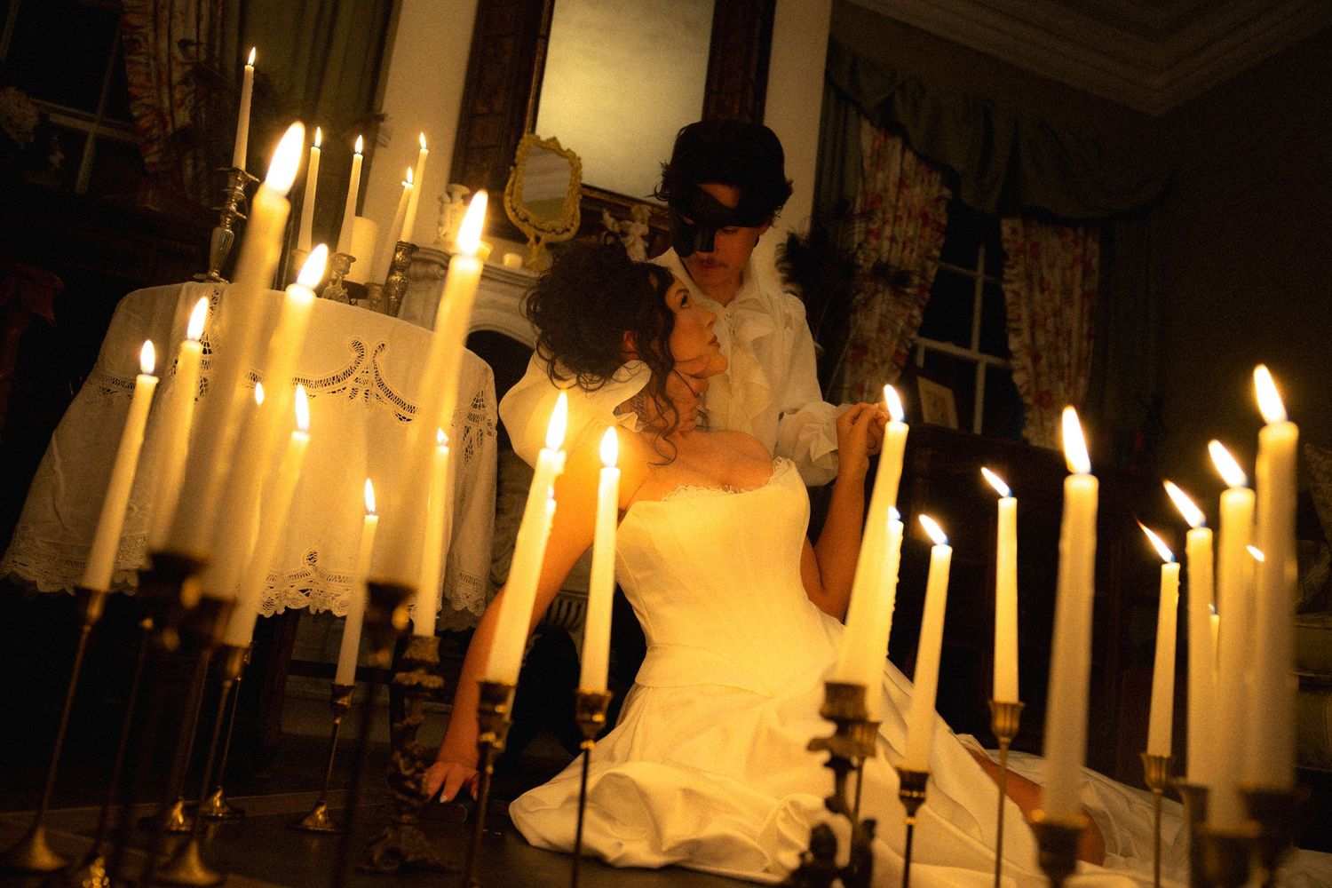 A romantic candlelit scene with white taper candles glowing warmly around a couple in formal wedding attire.