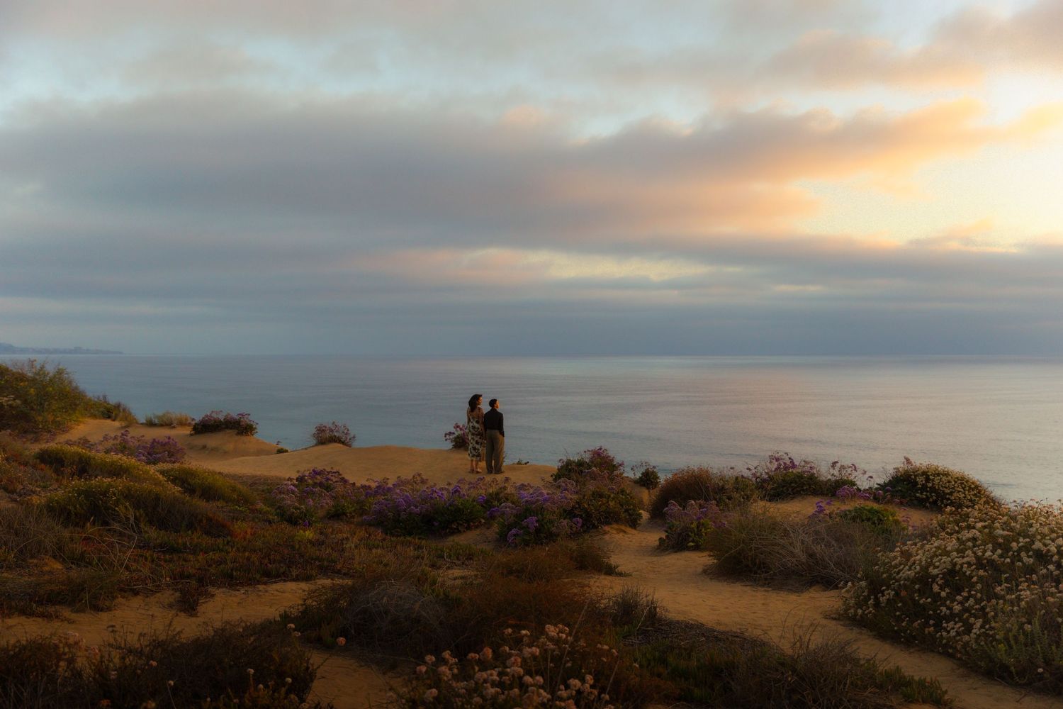 Silhouette of a couple taking in sunset views from coastal cliffs overlooking the Pacific Ocean.