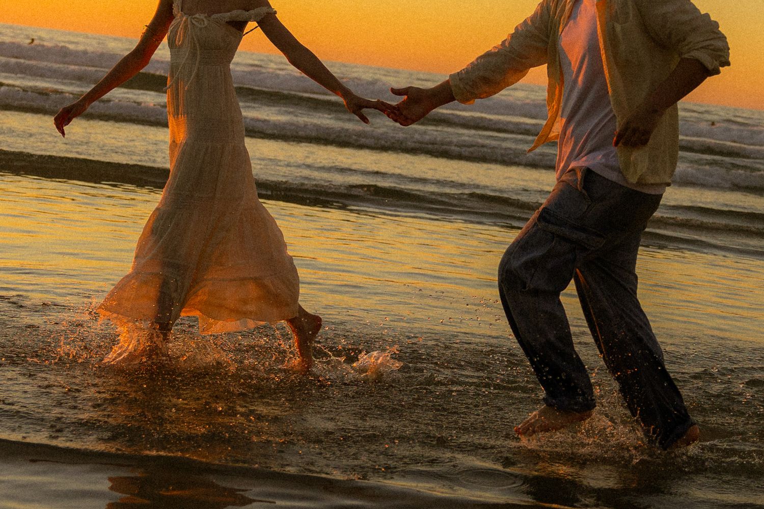 Silhouetted figures splash and play in shallow water during a vibrant orange sunset at the beach.