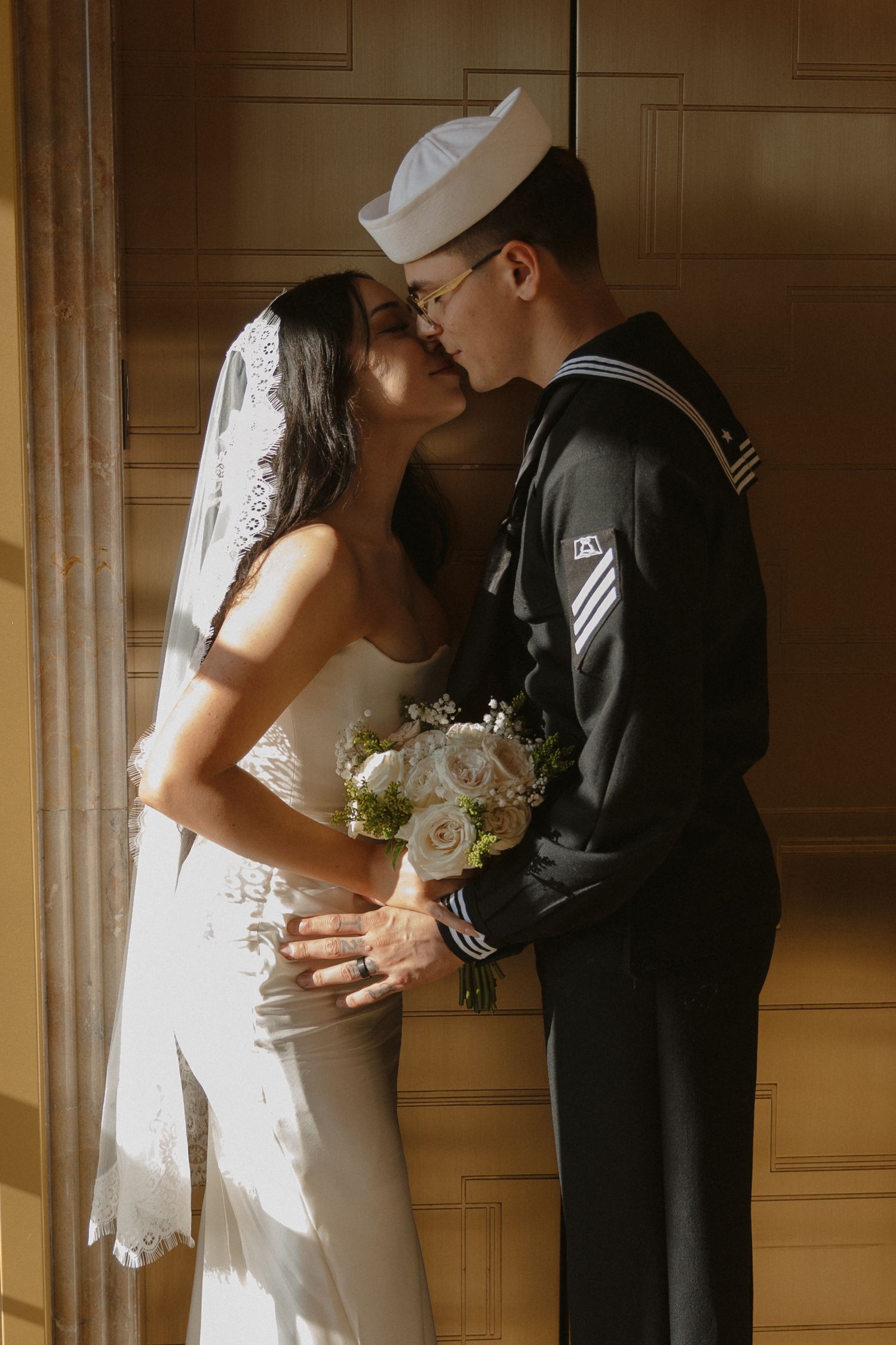 A romantic moment between a bride in white dress and naval service member in dress uniform, sharing a tender embrace.