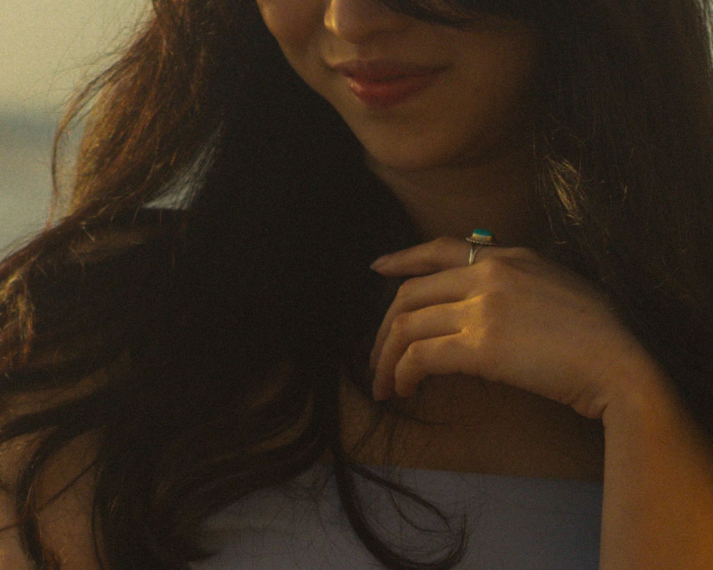 Closeup shot showing long dark hair and turquoise ring in warm sunlight.