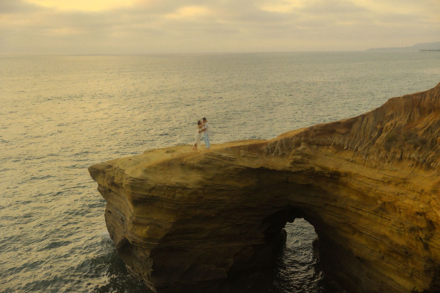 Dramatic coastal cliffs with natural stone arch formation at sunset over ocean.