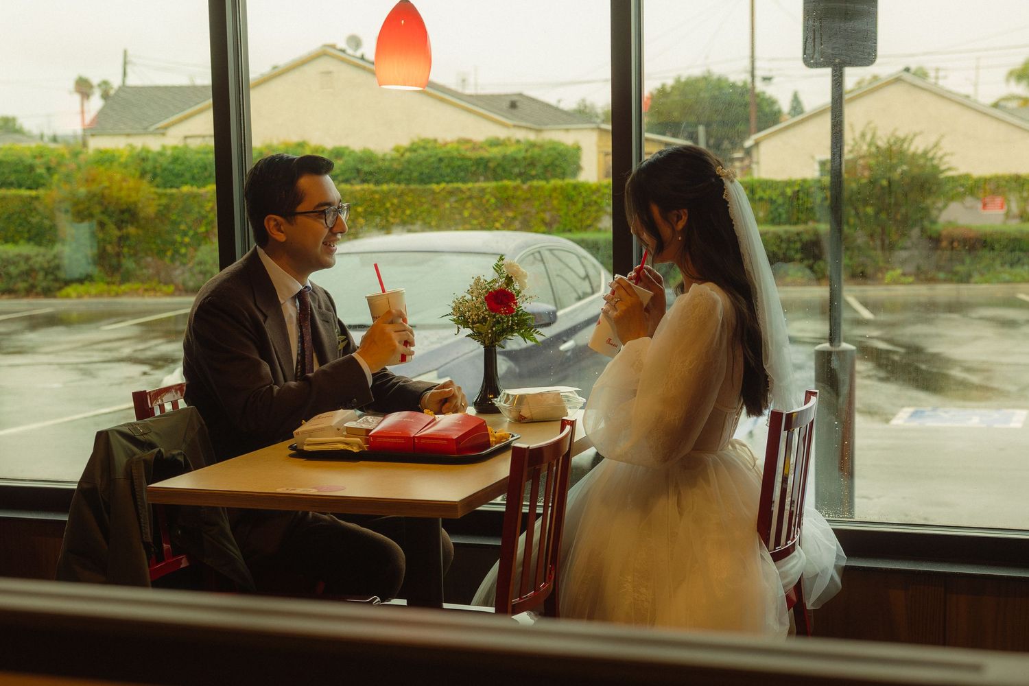 A group of diners sit at tables in a restaurant near large windows overlooking a rainy day outside.