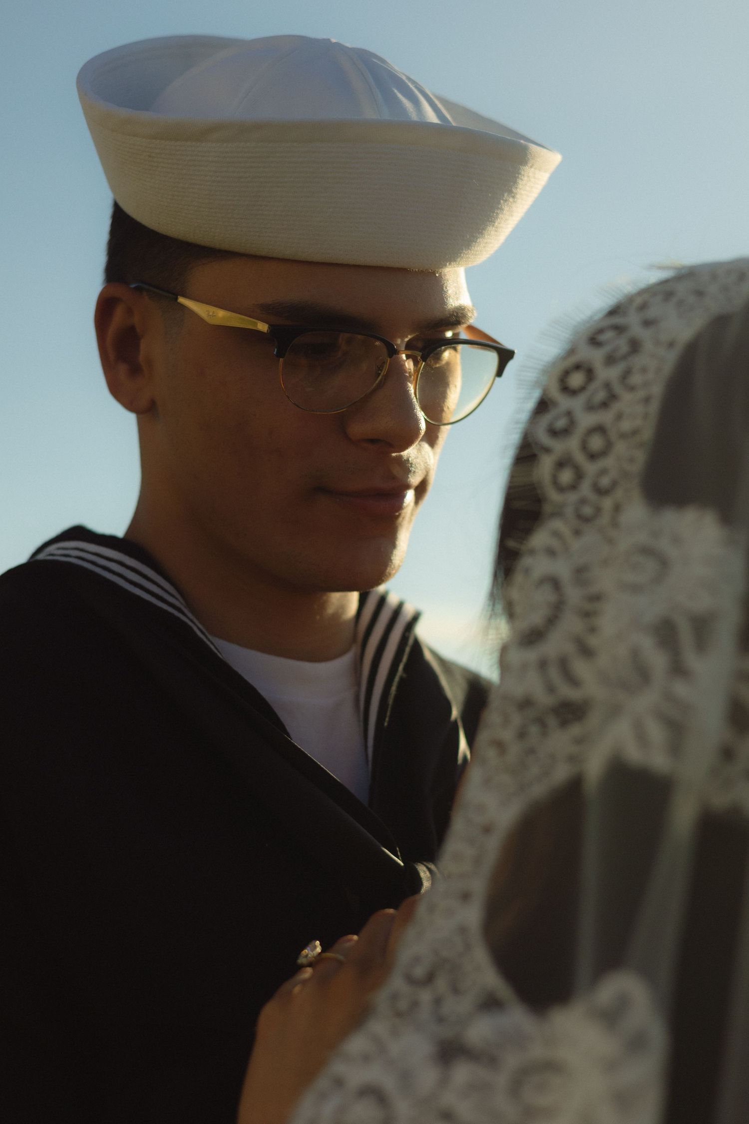 A sailor in dress whites and glasses stands in warm lighting at a wedding ceremony.