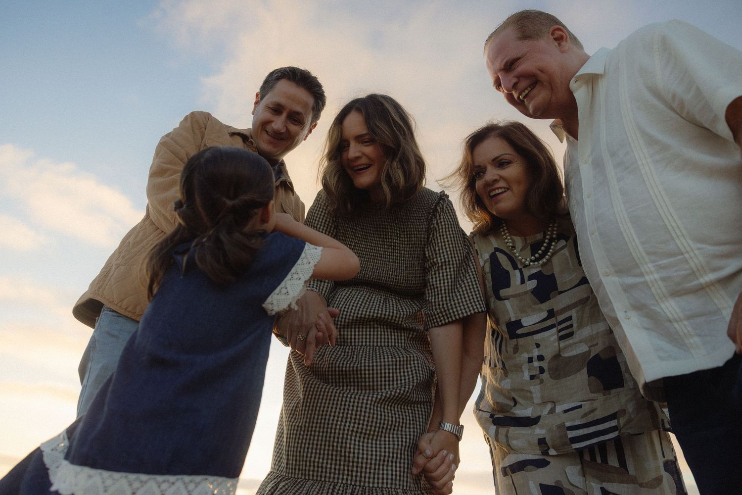 A group of people pose together from a low angle view against a bright sky background.