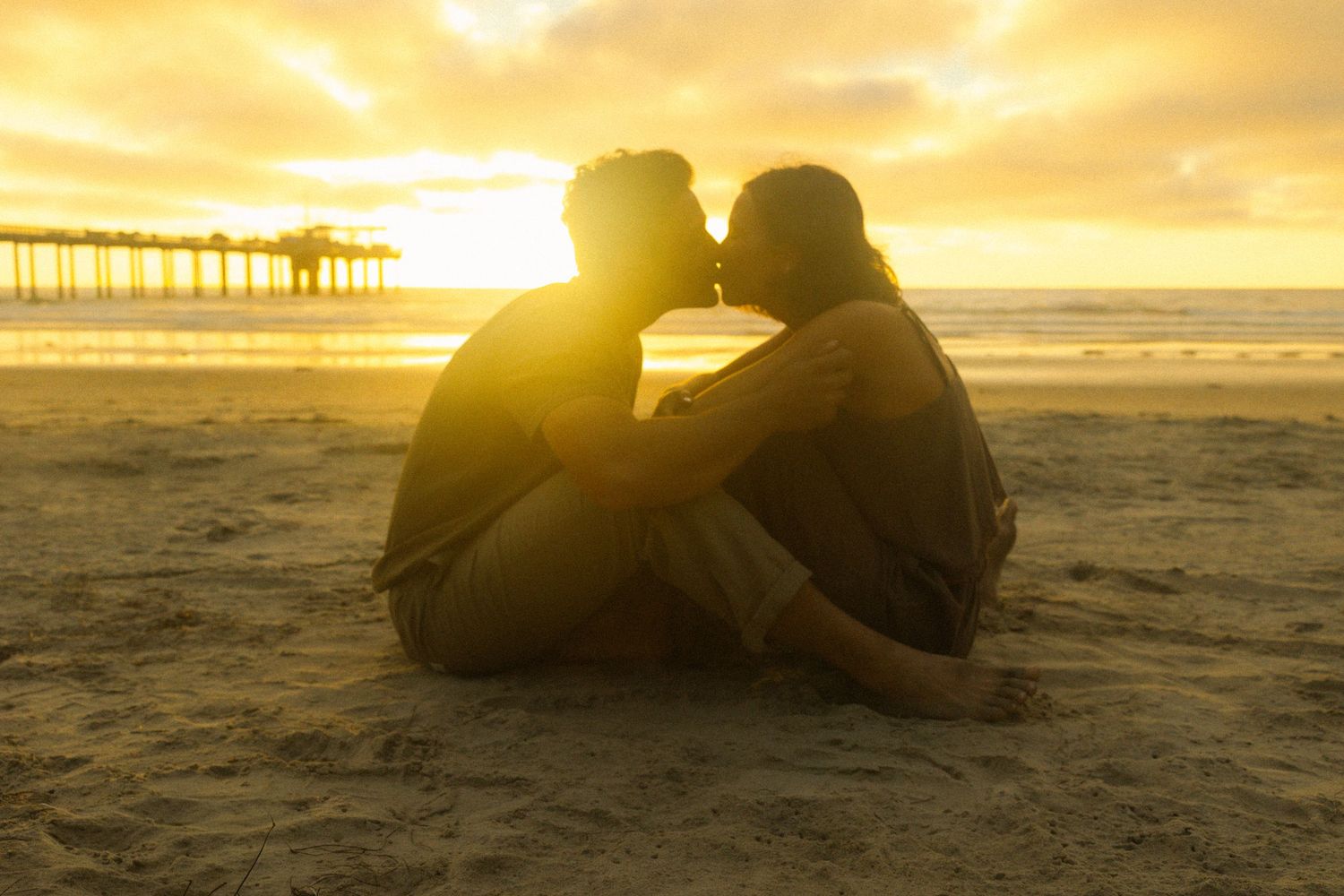 Silhouettes of people sitting on beach at sunset with golden sky and waves crashing in background.