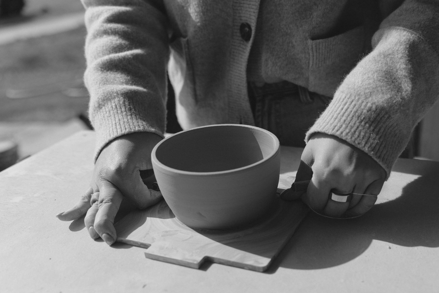 Hands placing a handmade ceramic bowl on a light surface in black and white.