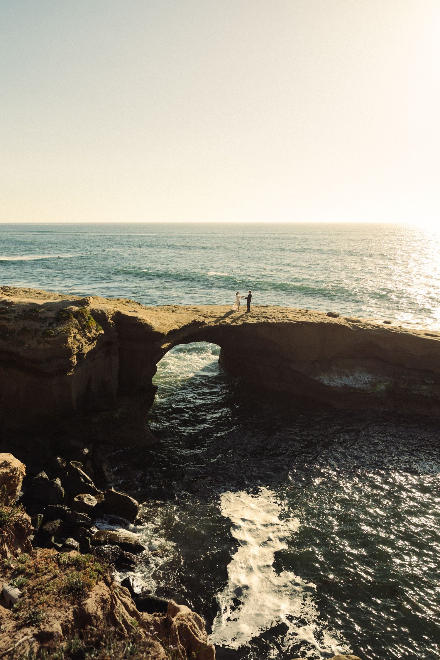 Dramatic coastal cliffs and rock formations frame the ocean waves crashing below at sunset.