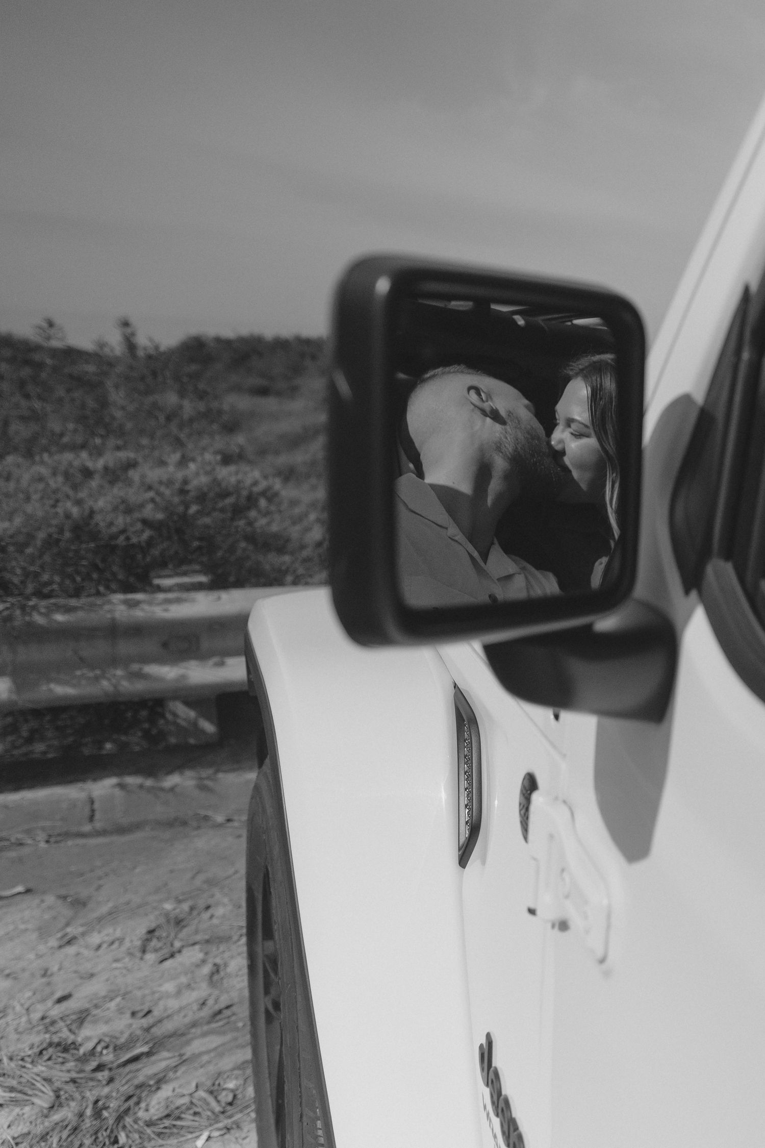 Black and white reflection of couple's intimate moment captured in car side mirror.