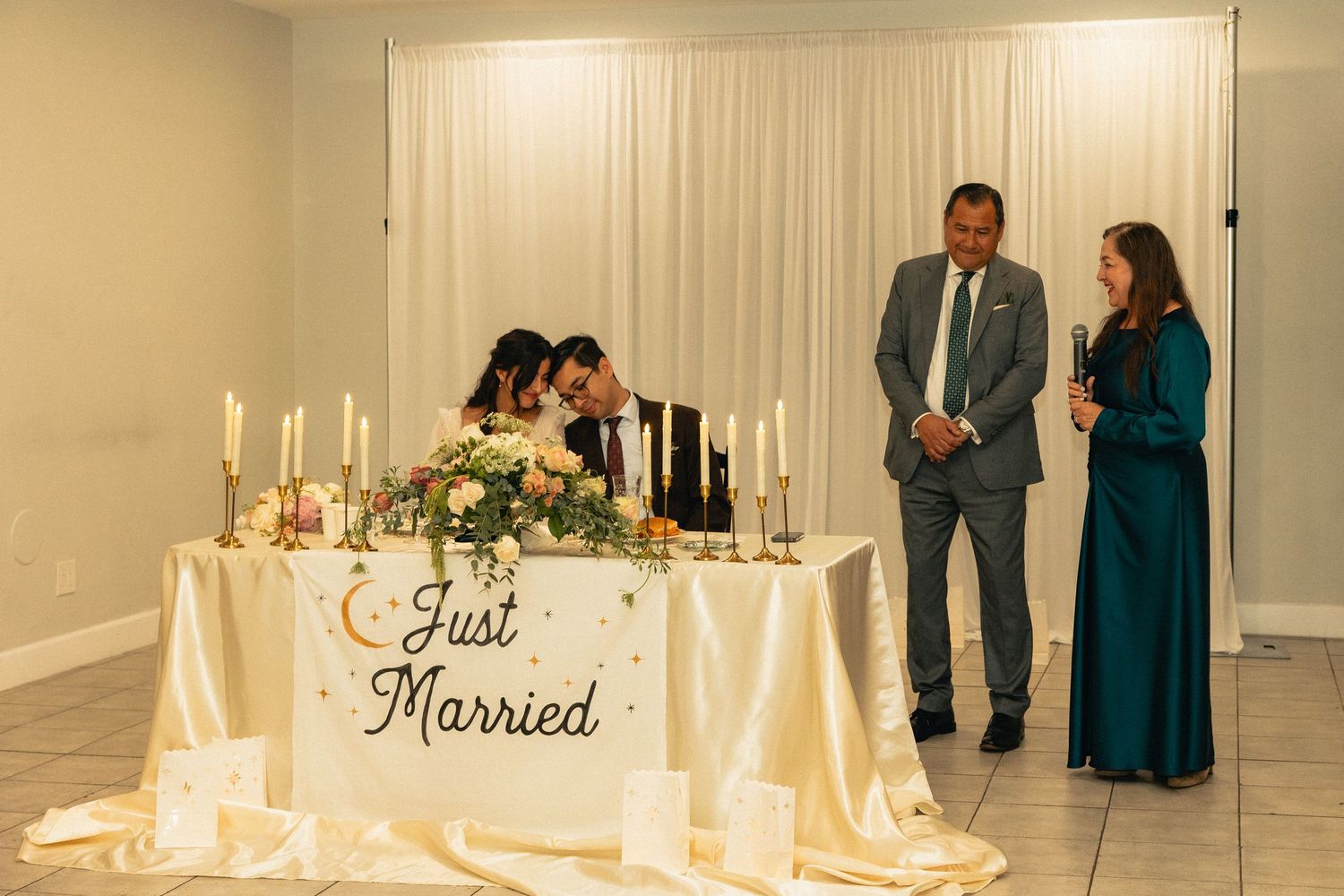 Wedding venue decorated with white curtains, floral arrangements and candlelight for an evening celebration.