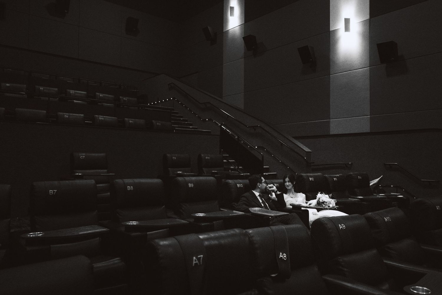 Empty dark movie theater with rows of seats illuminated by dim lighting from wall sconces.