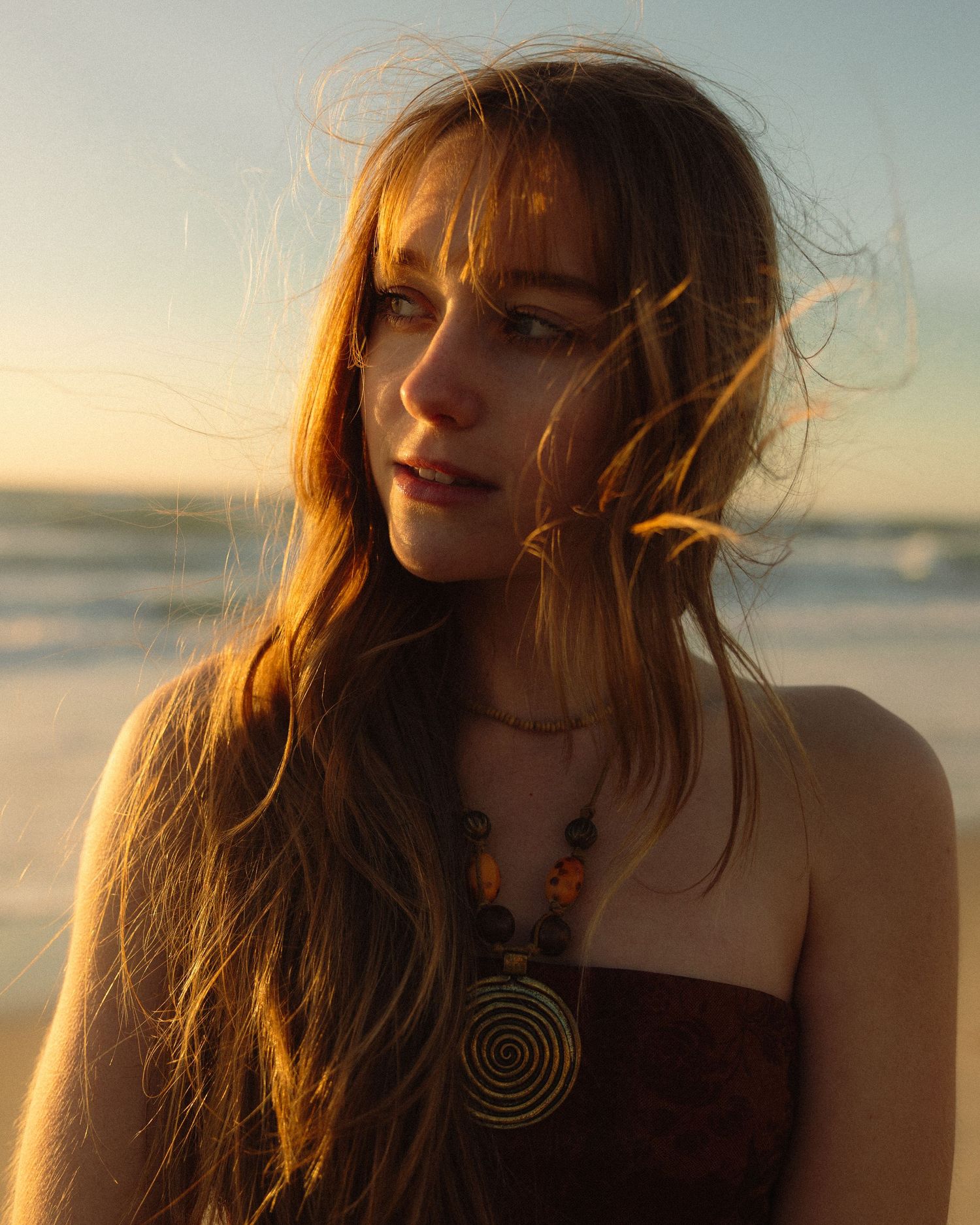 A person with windswept red hair stands against a sunset sky in a series of candid outdoor portrait shots.