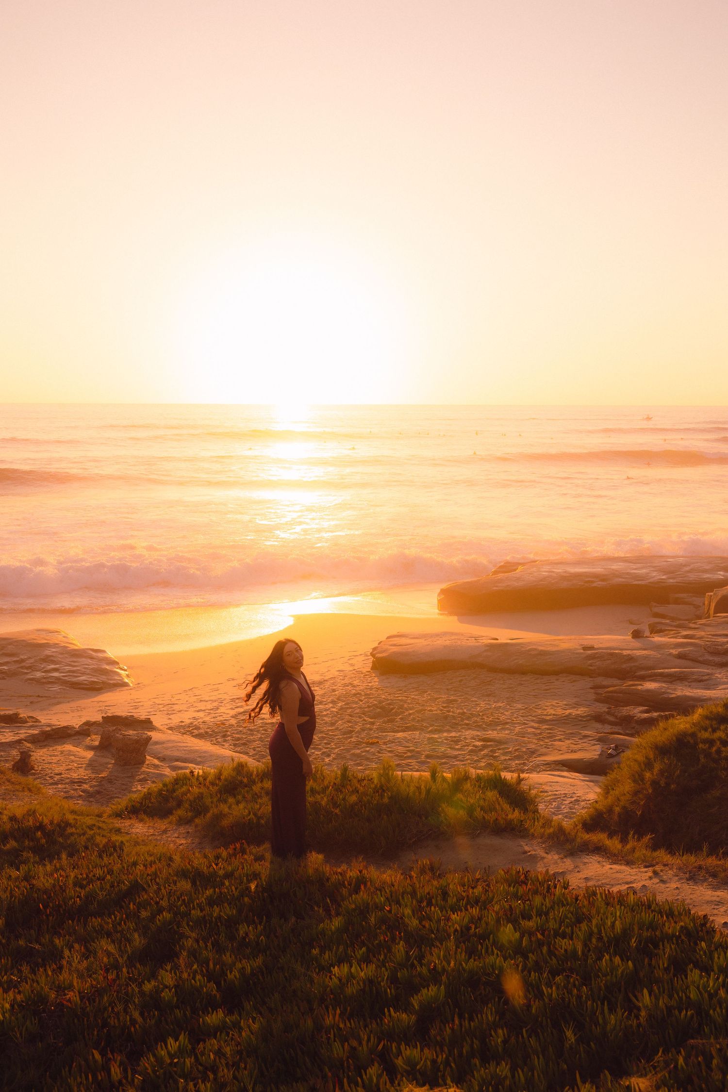 A silhouette stands on a cliff overlooking a dramatic coastal sunset with golden light illuminating the ocean landscape.
