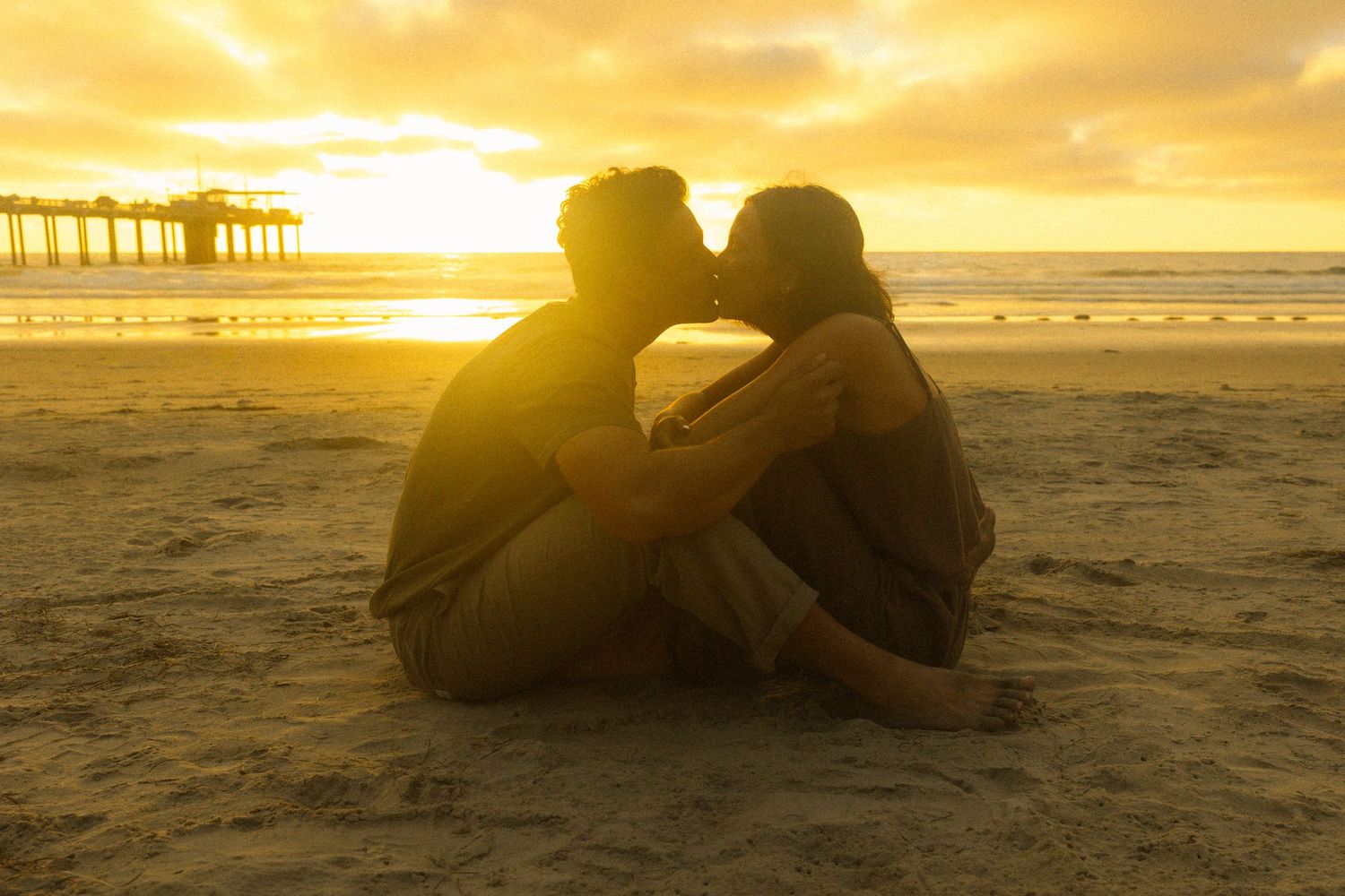 Two silhouettes embrace on a sandy beach at sunset with golden light streaming across the ocean waves.